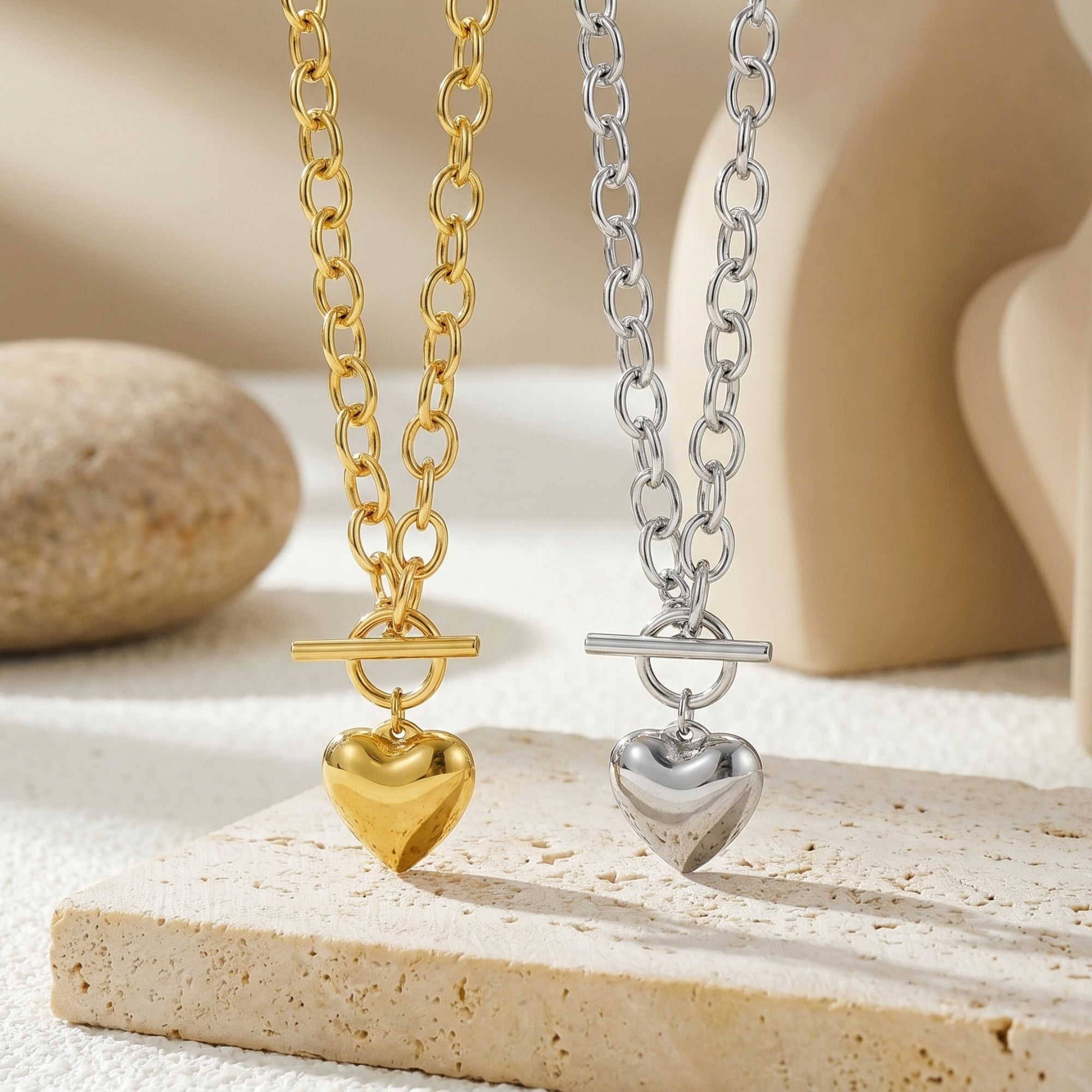 Gold and silver heart pendant necklaces with toggle clasps on a textured stone surface.