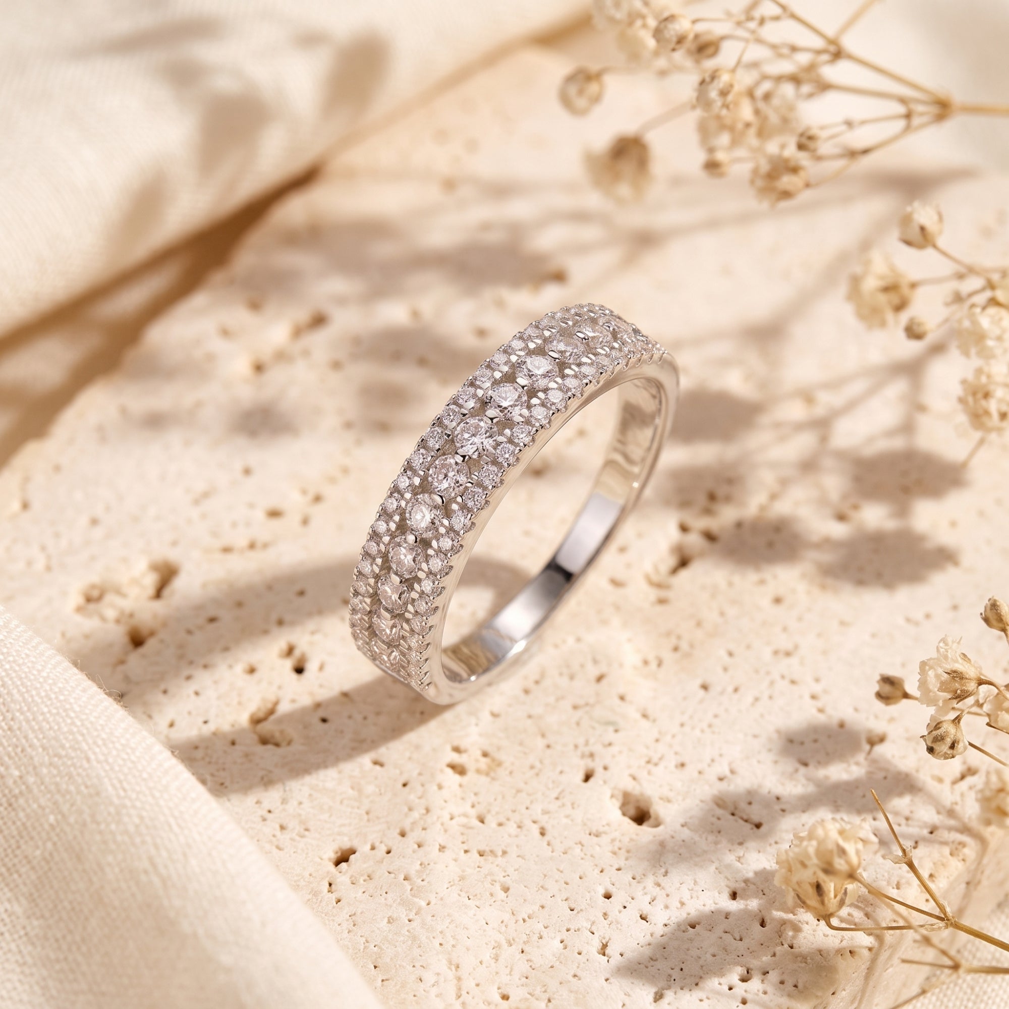 Three-row simulated diamond sterling silver ring on stone with dried flowers.
