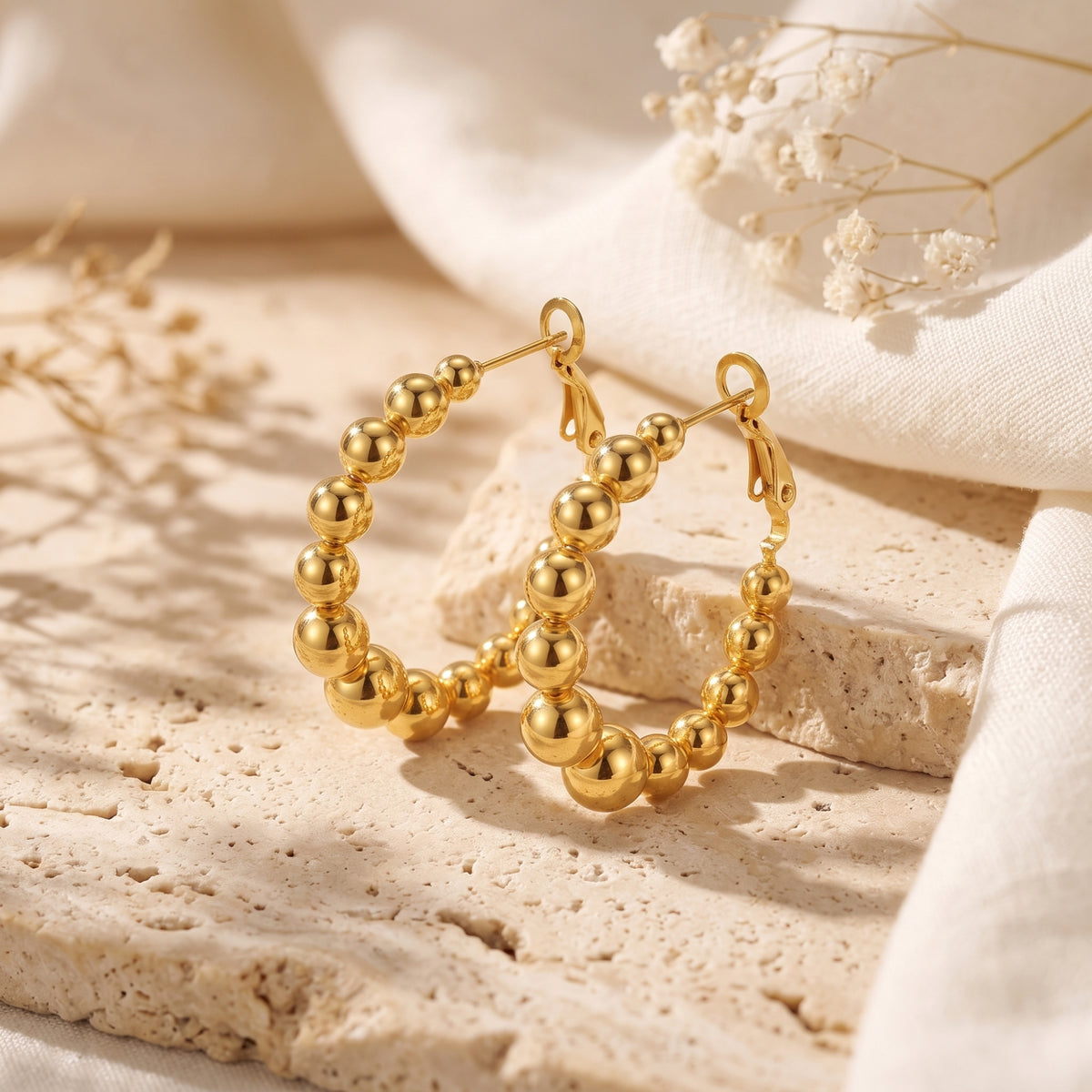 Pair of gold-colored graduated beaded hoop earrings displayed upright on textured stone blocks.