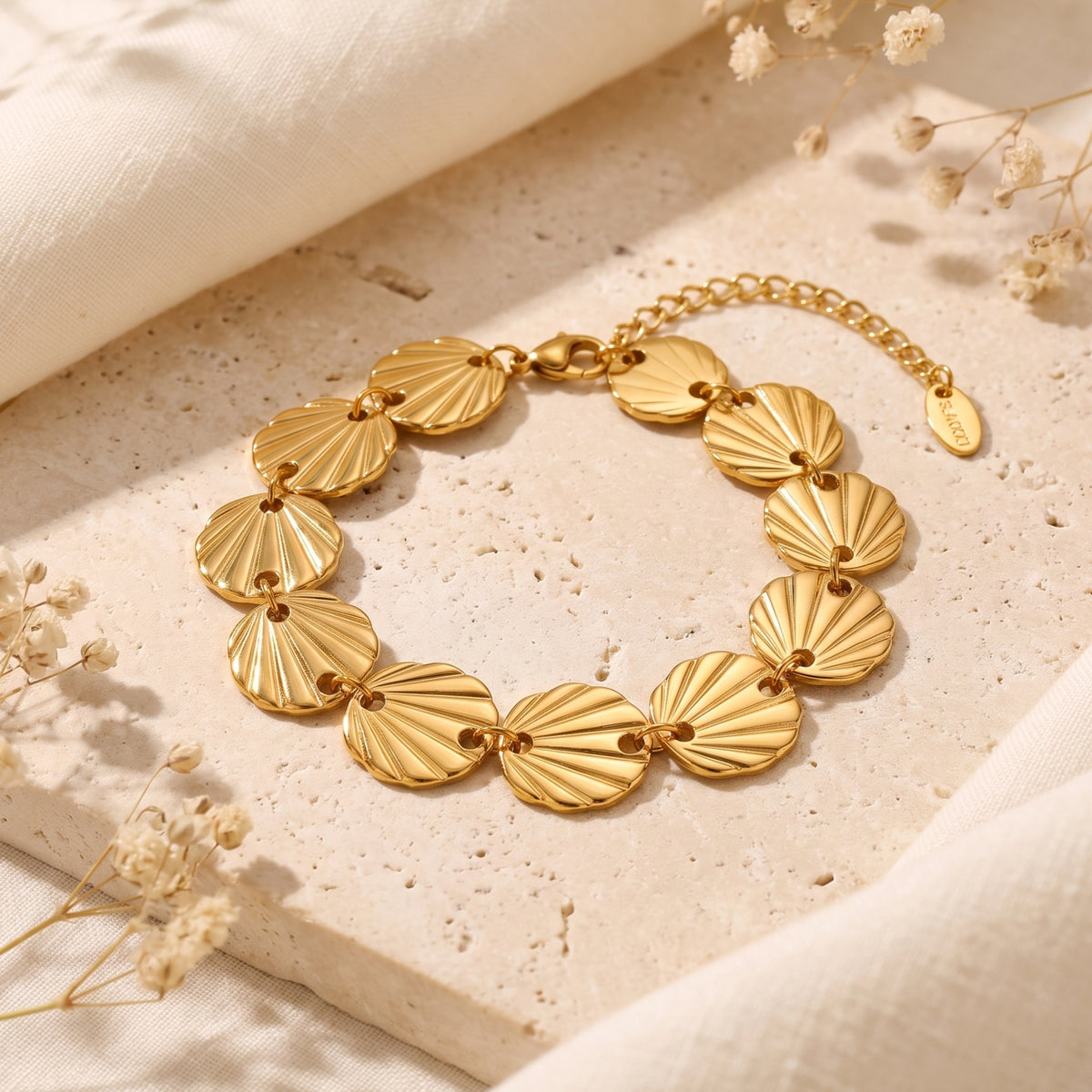 Gold-tone seashell link bracelet arranged in a ring on a textured stone slab with dried flowers