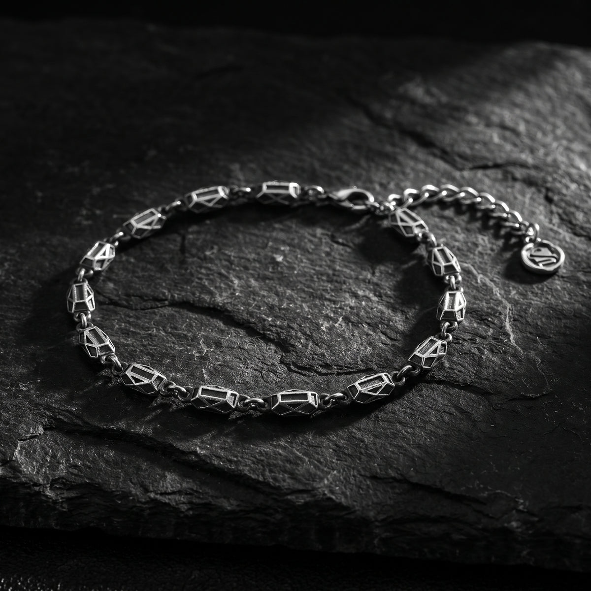 Silver geometric link bracelet arranged on dark slate, with its extension chain and clasp visible.