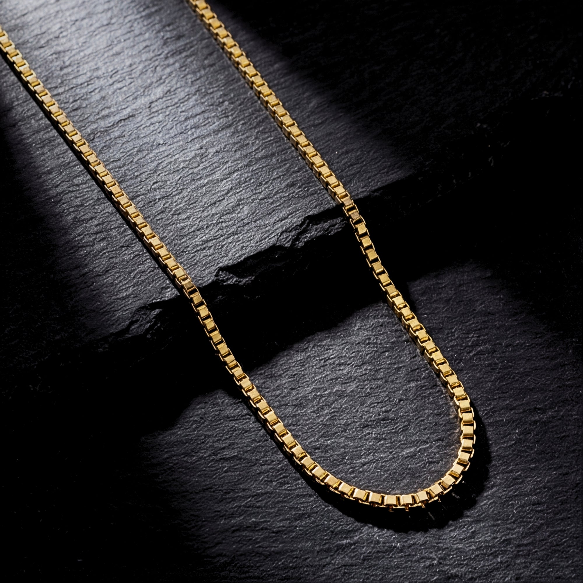 18k gold bonded stainless steel Boxed In box chain for men on a dark, textured stone surface.