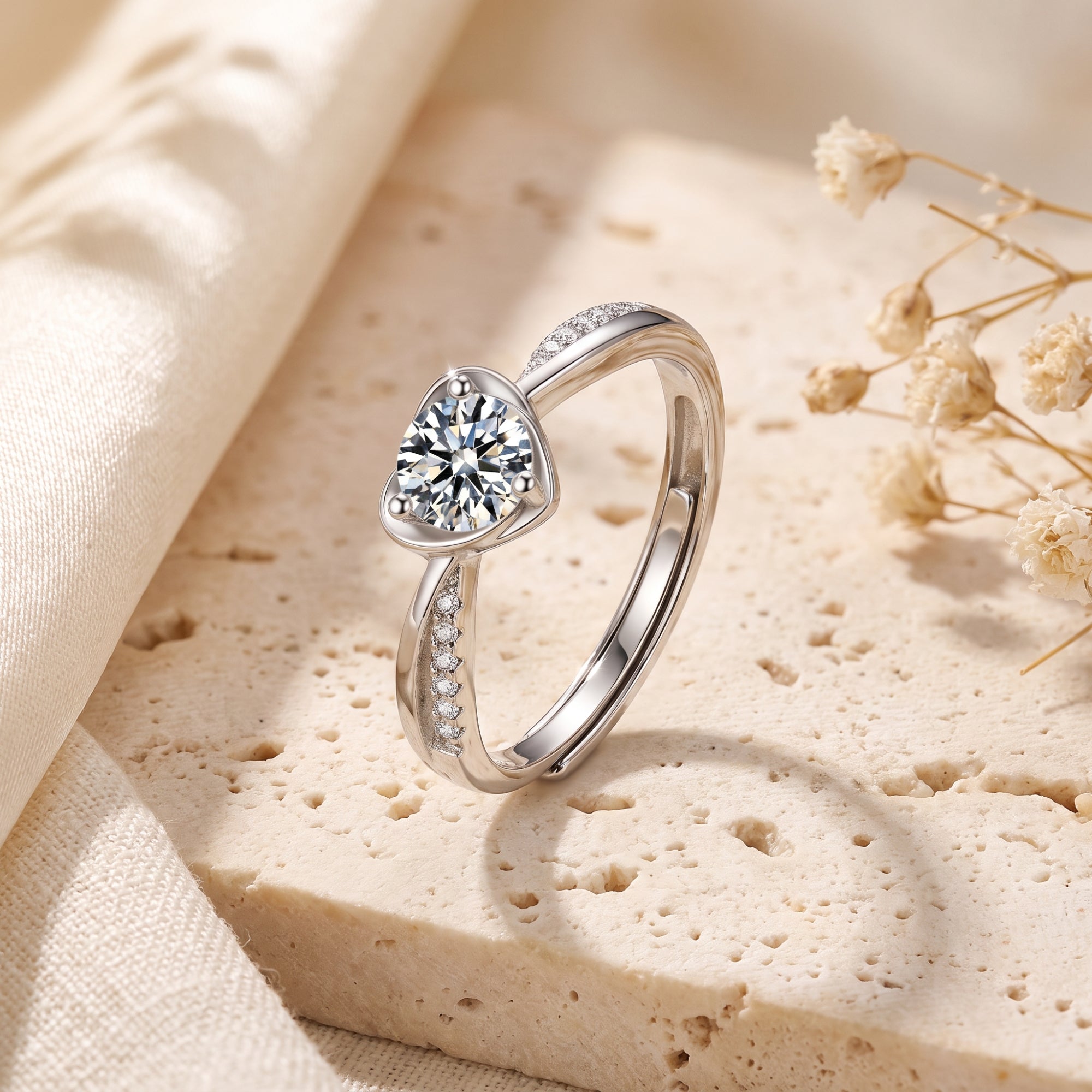 Sterling silver heart bypass ring with round simulated diamond on a textured stone lifestyle background.