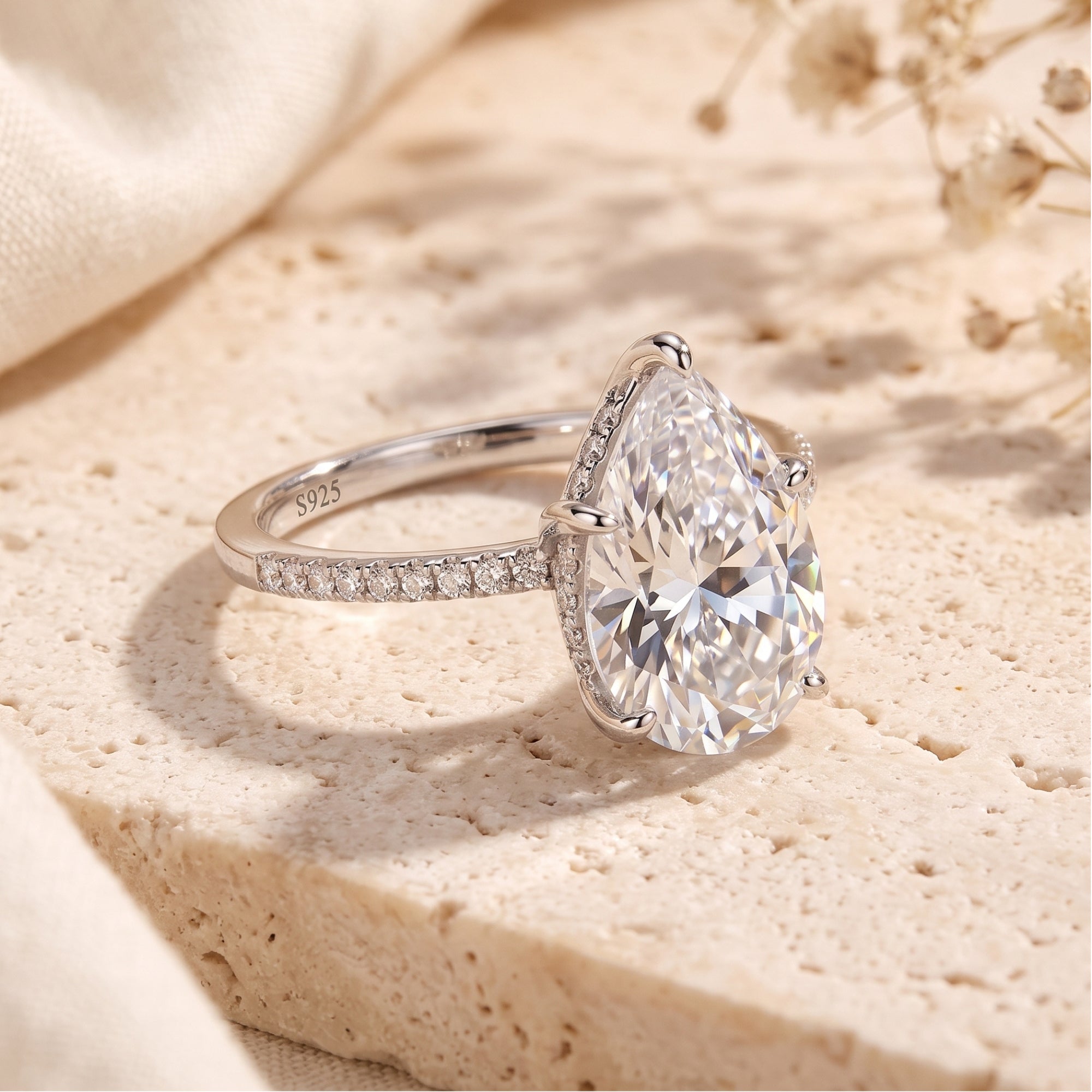 Pear-cut simulated diamond ring in S925 sterling silver with pavé band on a textured stone surface.