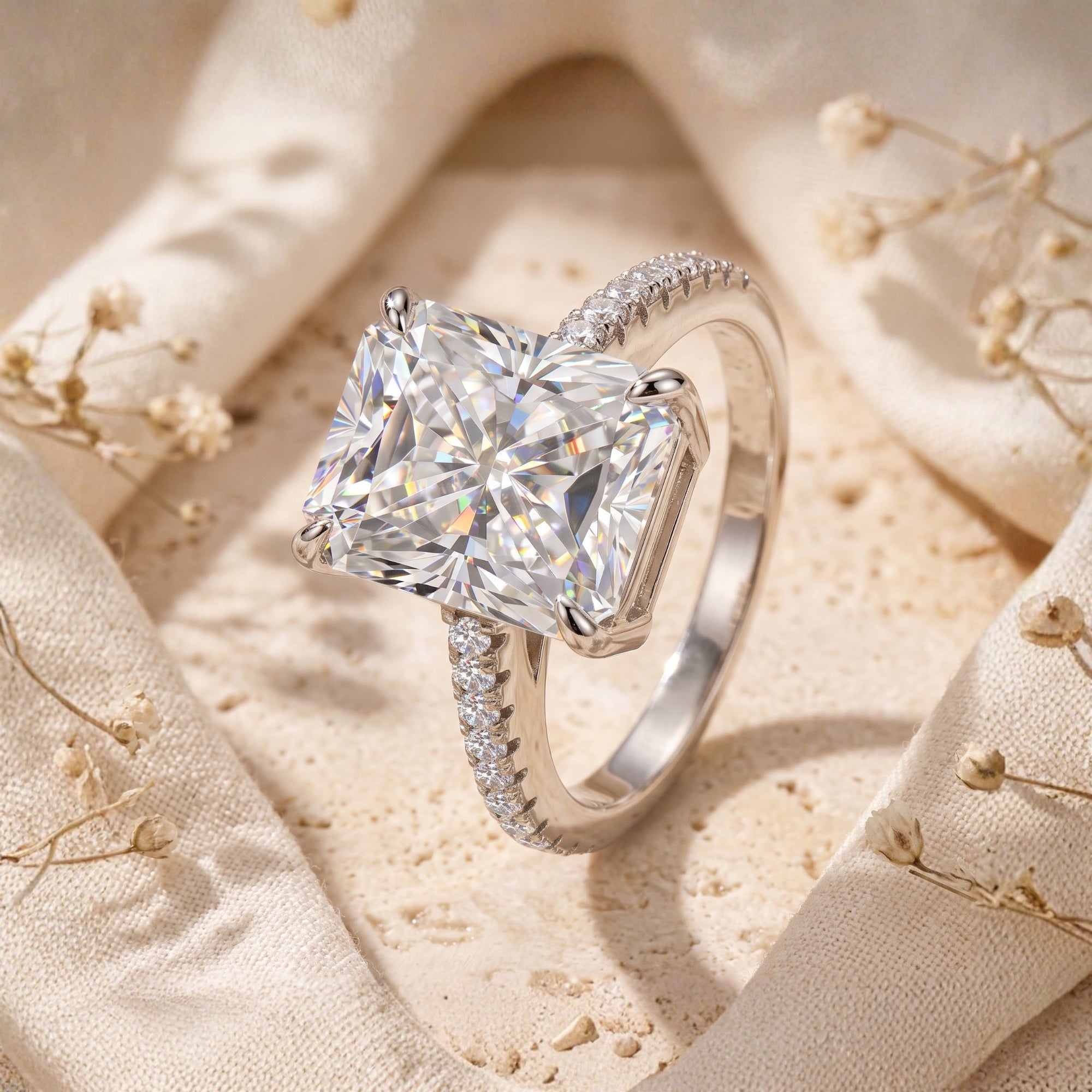 Radiant-cut CZ sterling silver Claudette promise ring with a pavé band, styled on cream fabric with flowers.