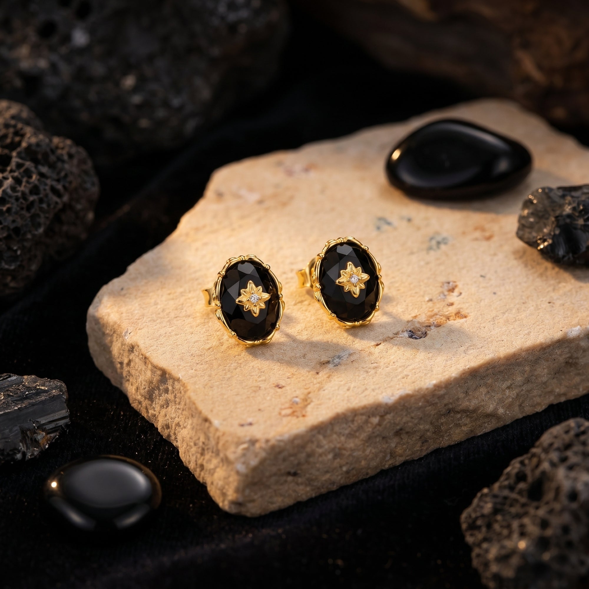 Yellow gold oval-cut faceted black onyx earrings displayed on a natural stone lifestyle background.