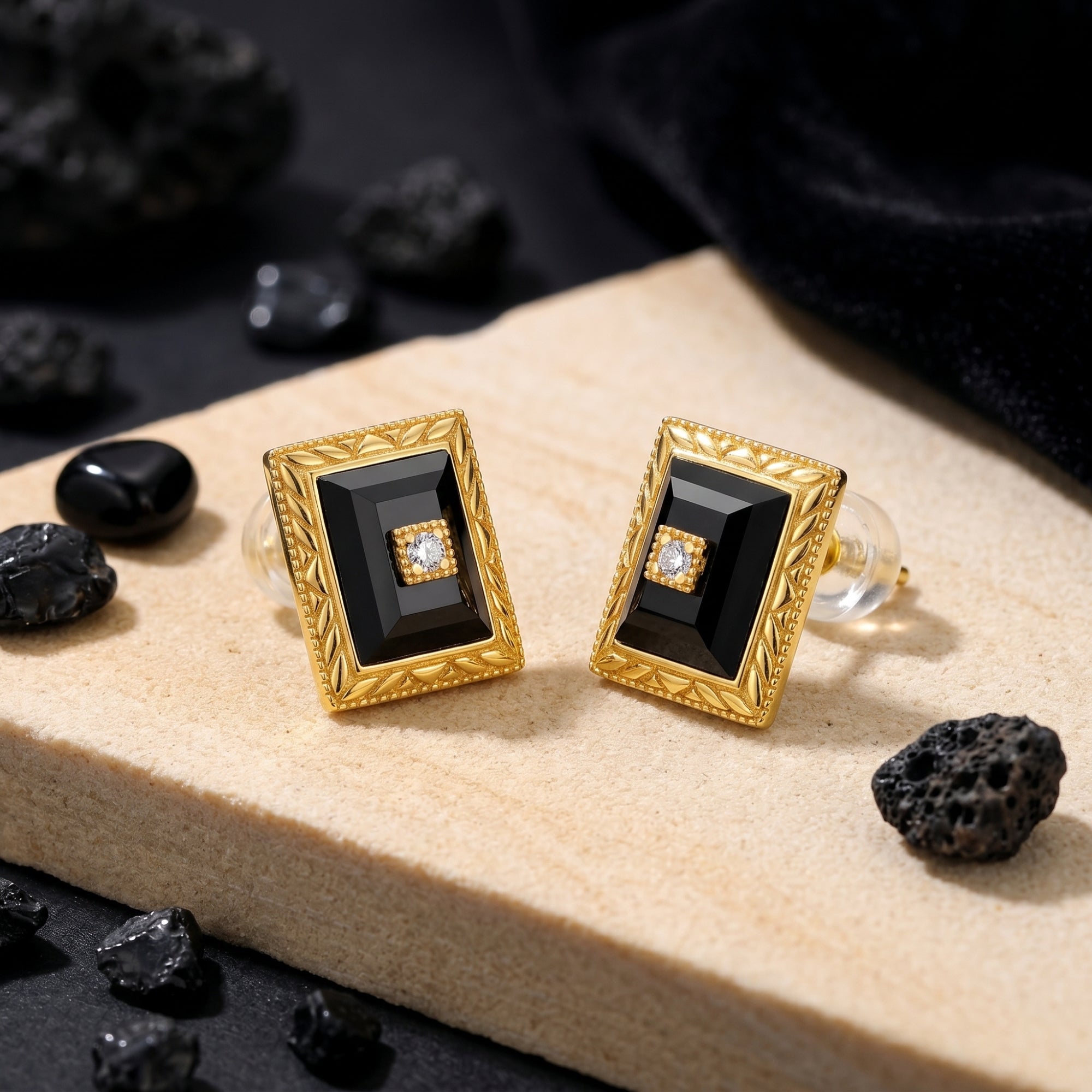 Yellow gold square-cut black onyx stud earrings with center diamond accent on a stone slab lifestyle background.