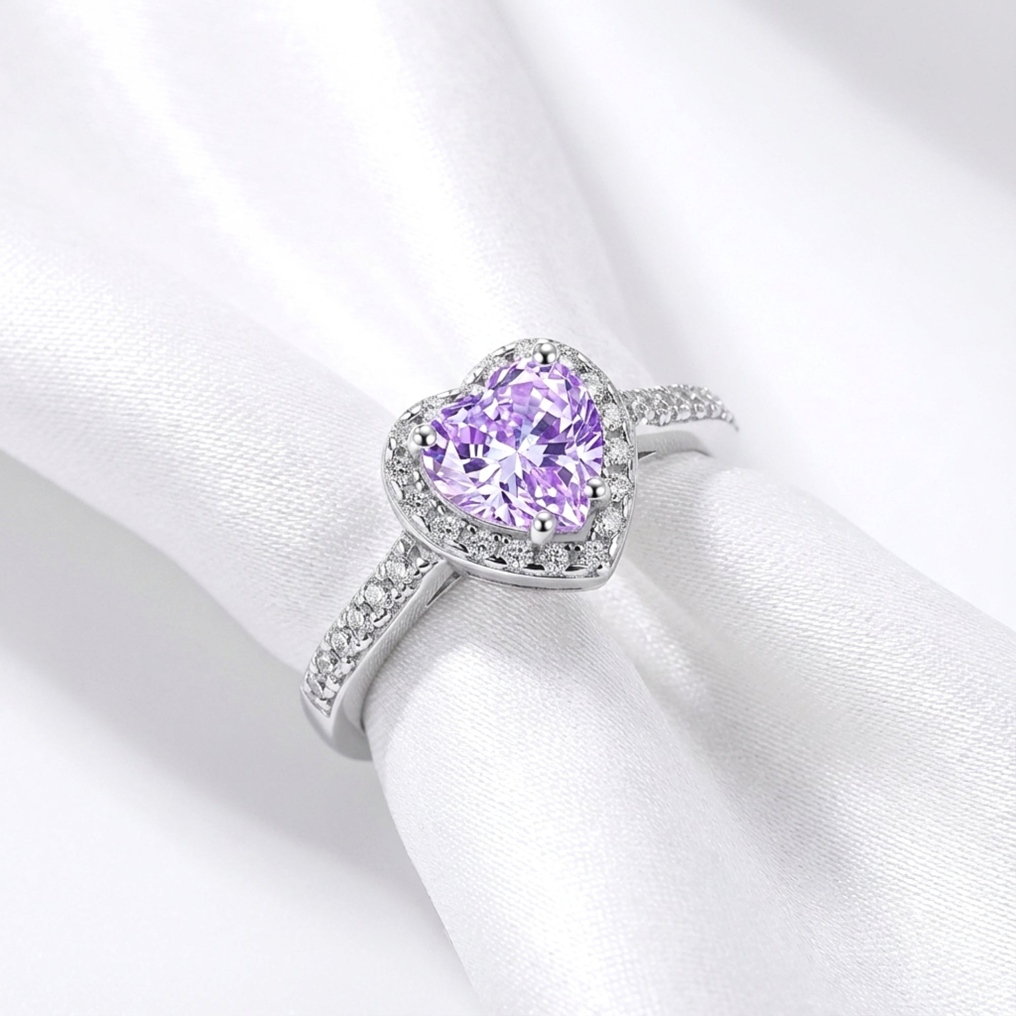 Angled top view of the heart-cut simulated amethyst halo ring in S925 sterling silver on white draped fabric.