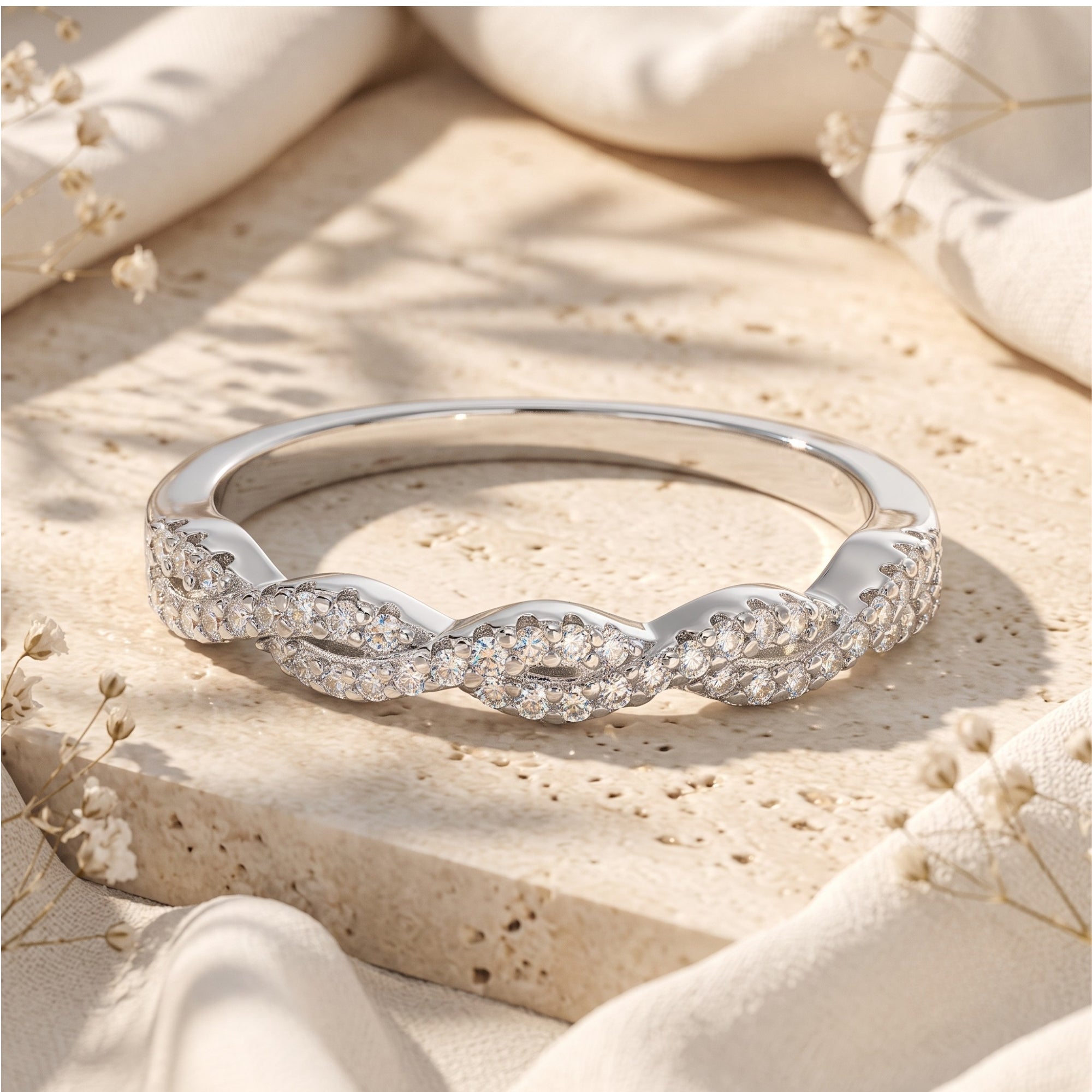 Helena twisted silver eternity ring with round simulated diamonds on a stone and floral lifestyle background.