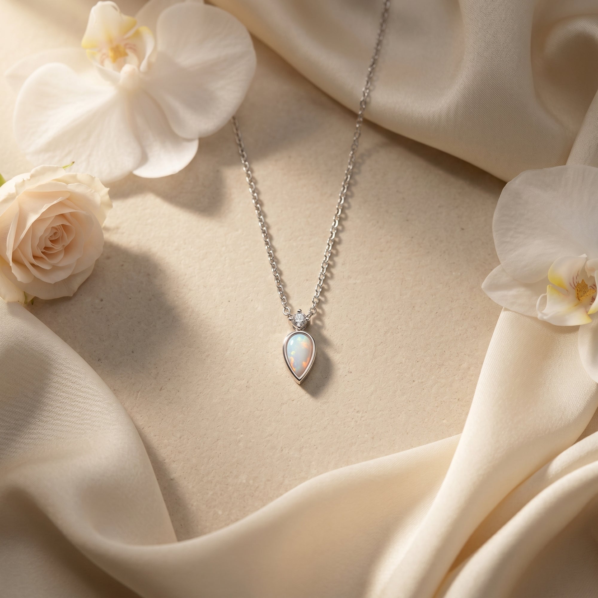 Silver teardrop white opal necklace with diamond accent on cream fabric with white orchids.