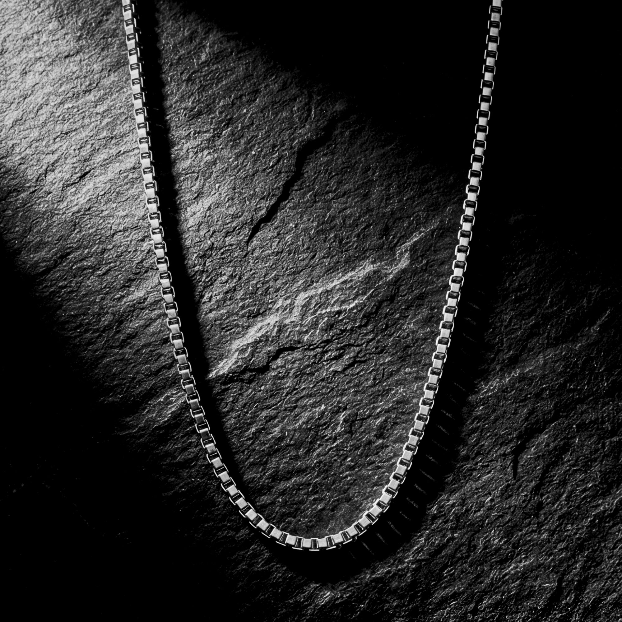 Silver stainless steel boxer chain necklace displayed on a dark textured stone background.