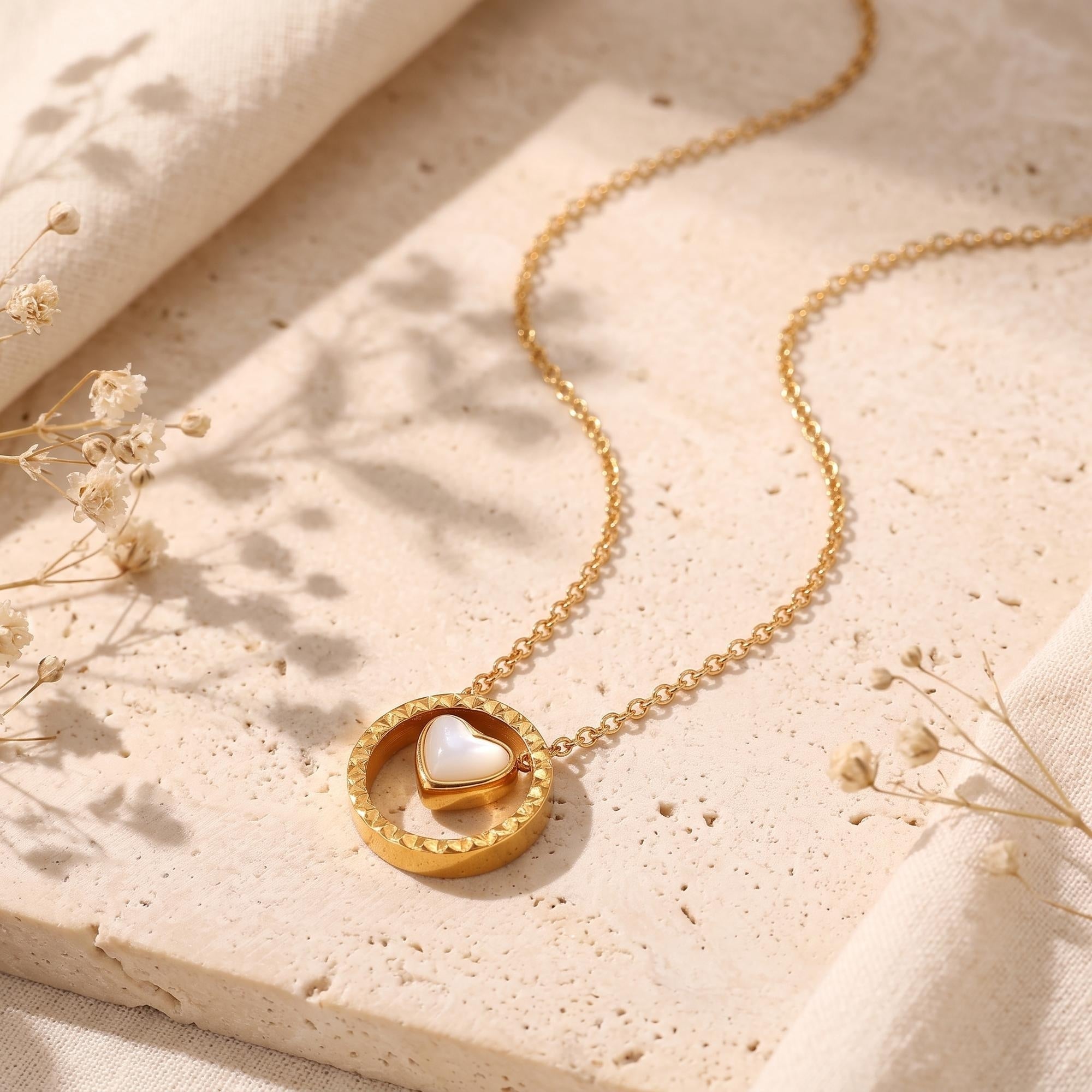 Gold Rosetta necklace with heart mother of pearl in textured circle on stone with dried flowers.