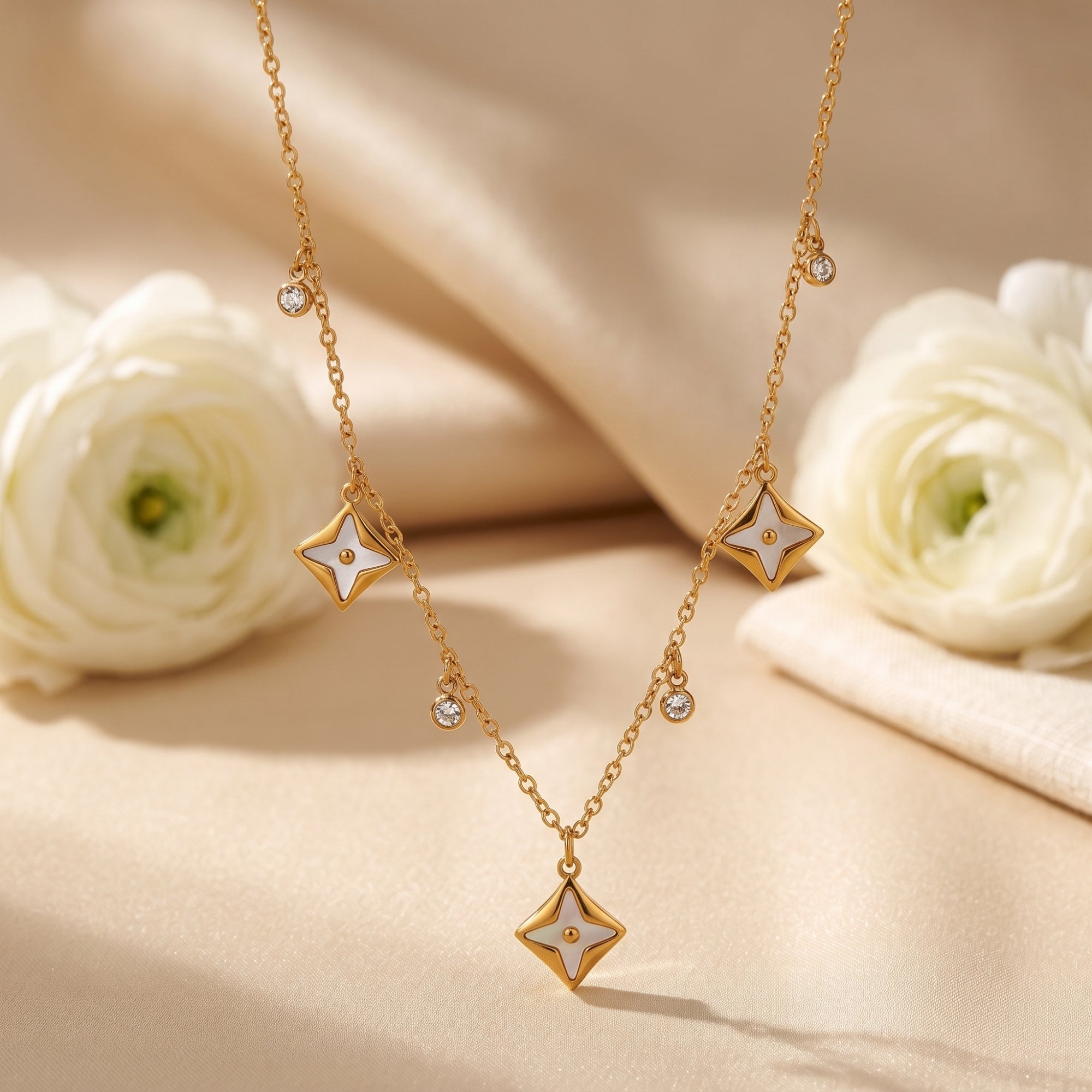 Gold star pendant necklace with white inlays and round crystals on draped fabric with white flowers.