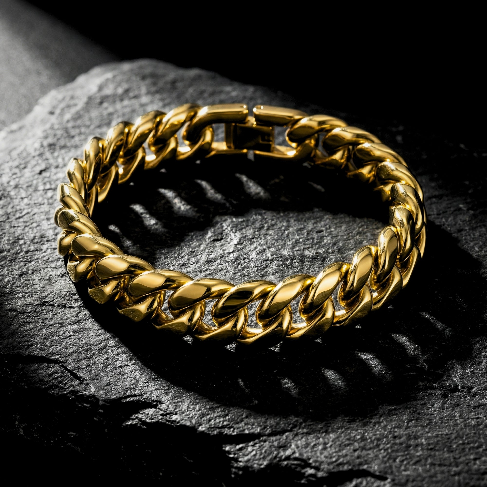Gold stainless steel Cuban link bracelet displayed on a dark textured rock surface.