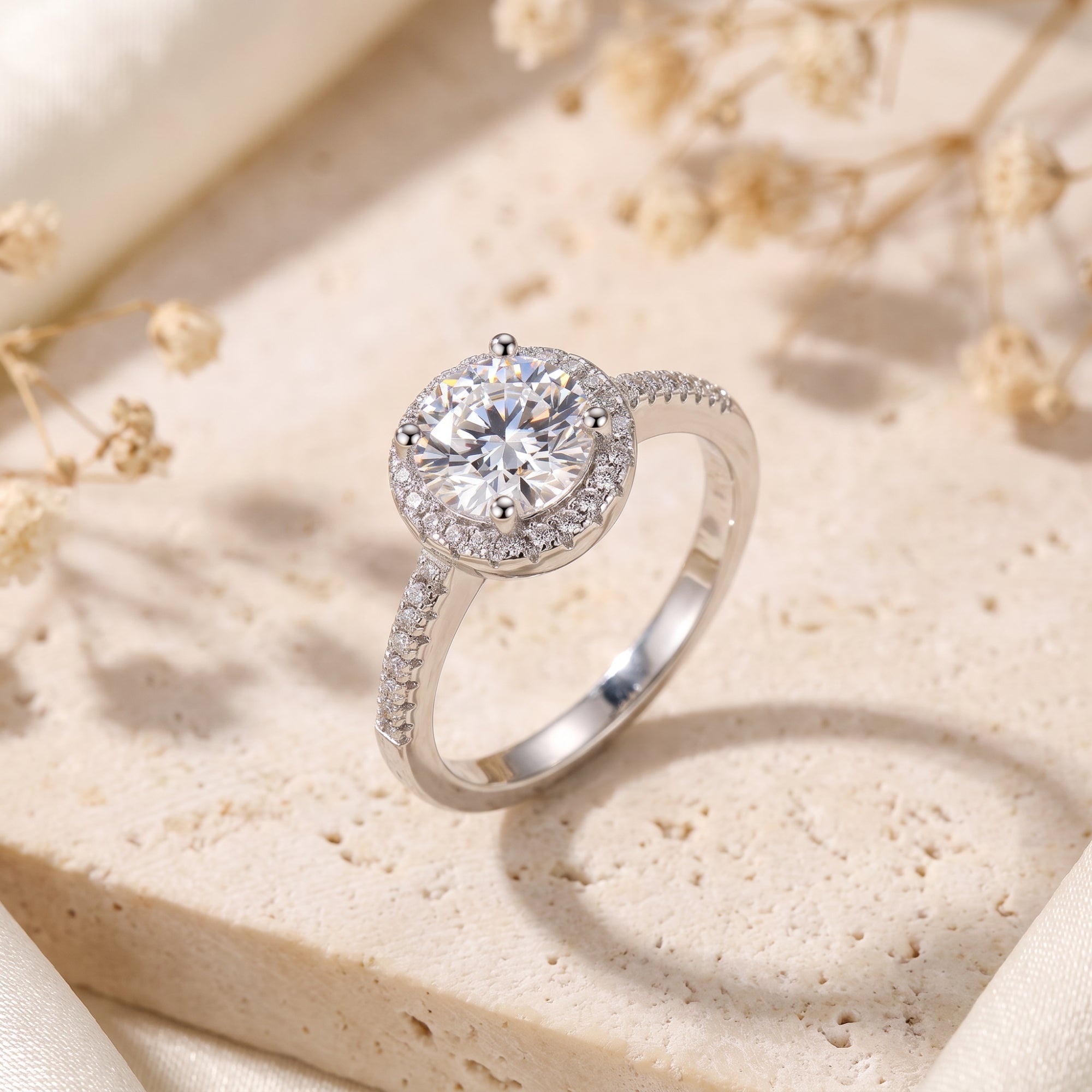 Sterling silver halo ring with a round-cut simulated diamond on a stone surface with dried flowers.