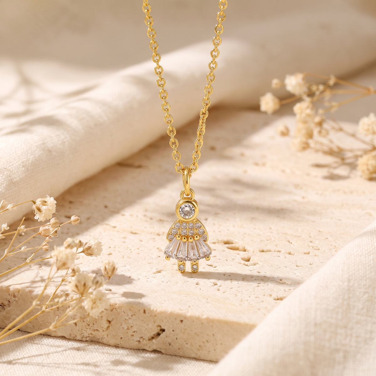 Frontal view of the gold-tone girl pendant necklace with clear simulated diamond accents on a stone surface.