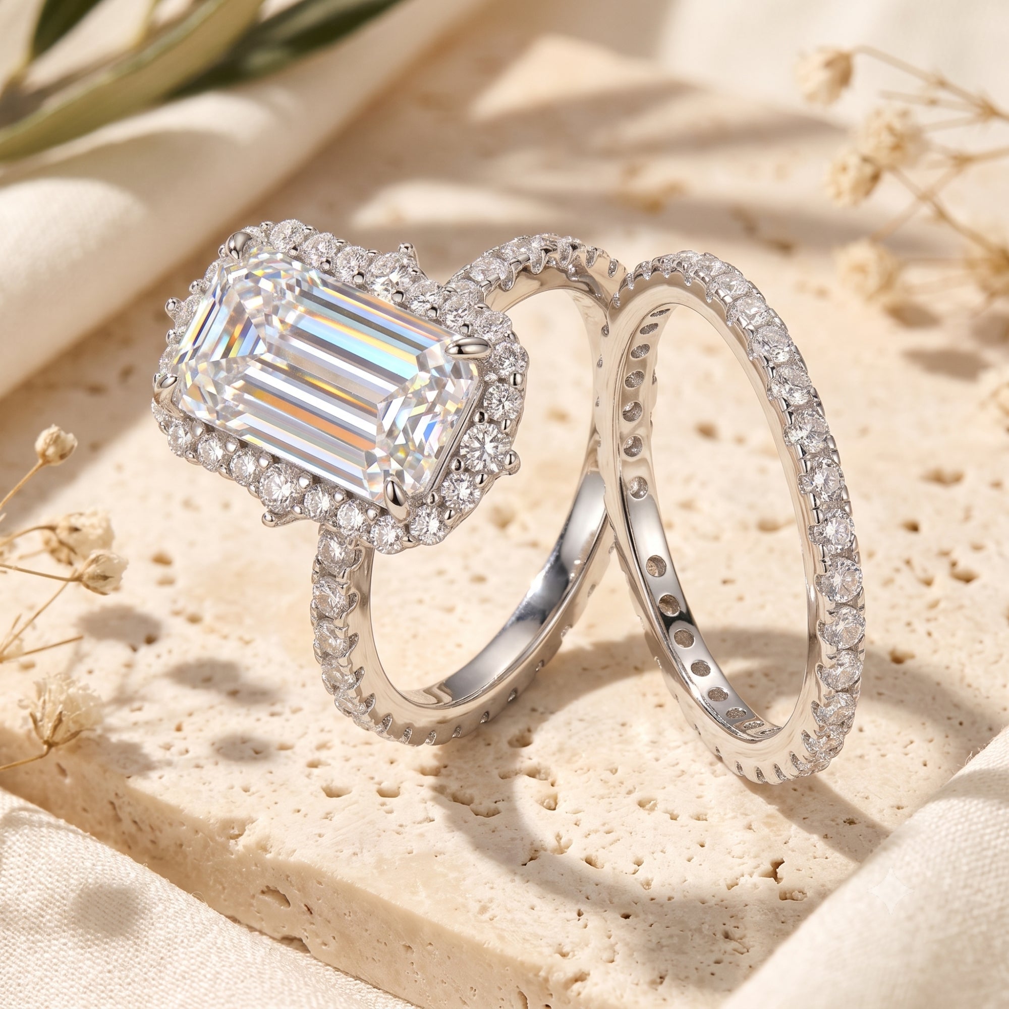 Silver halo ring set with emerald-cut simulated diamond on stone background with dried flowers.