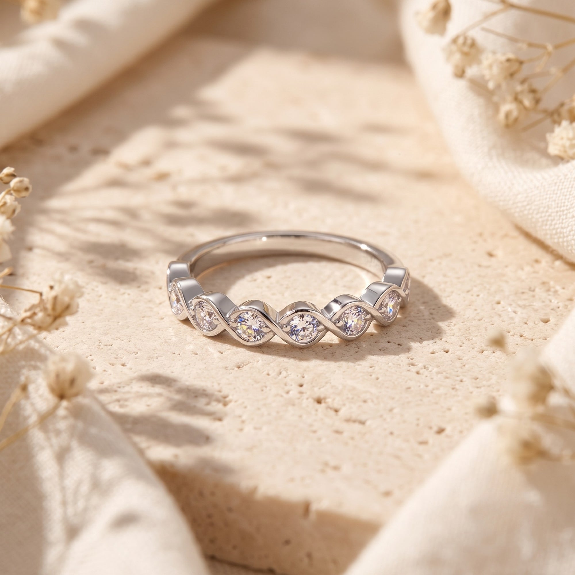 Amandelle sterling silver wave ring with round-cut simulated diamonds on a stone surface with dried flowers.