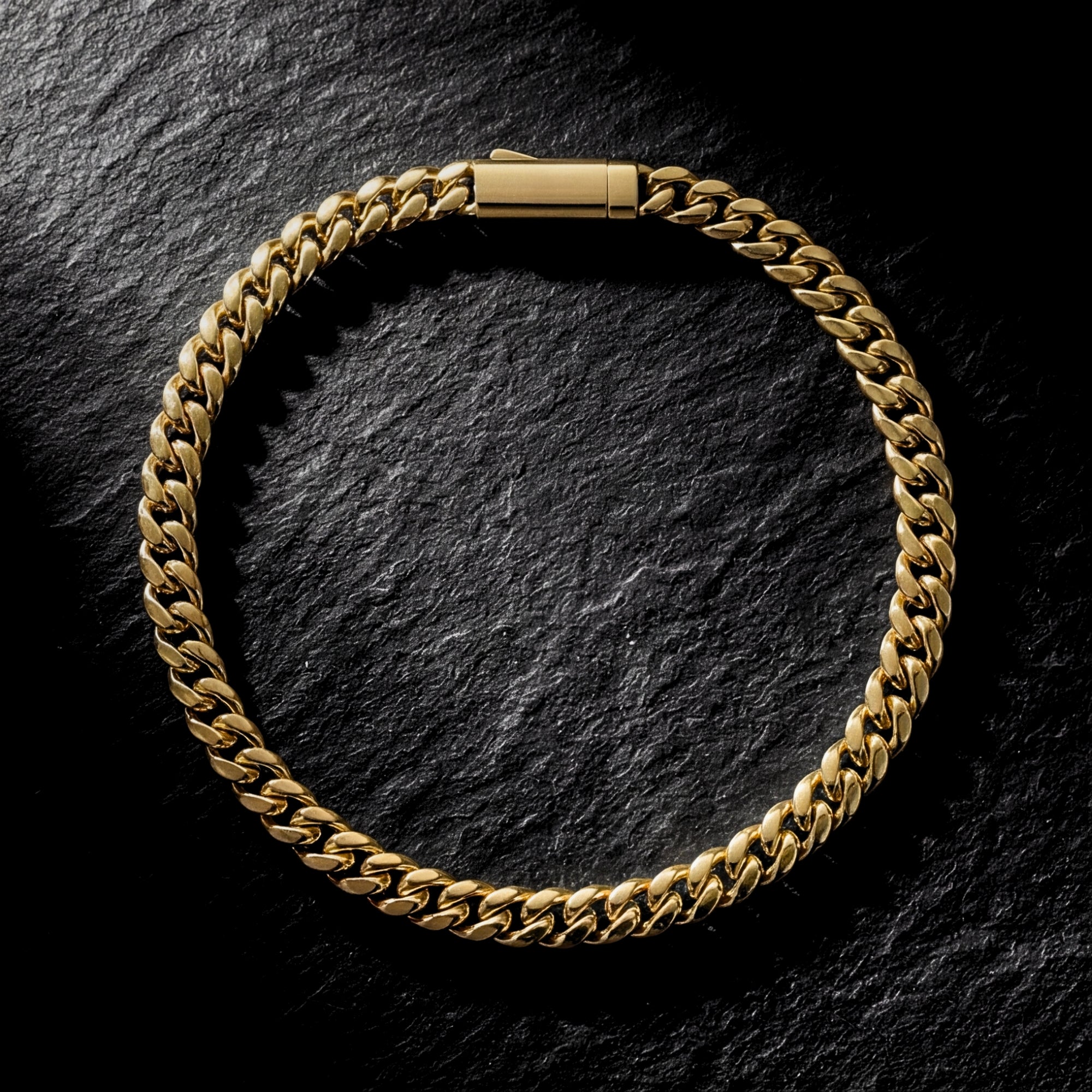 Gold stainless steel 5mm Cuban link bracelet laid flat in a circle on a dark textured stone background.