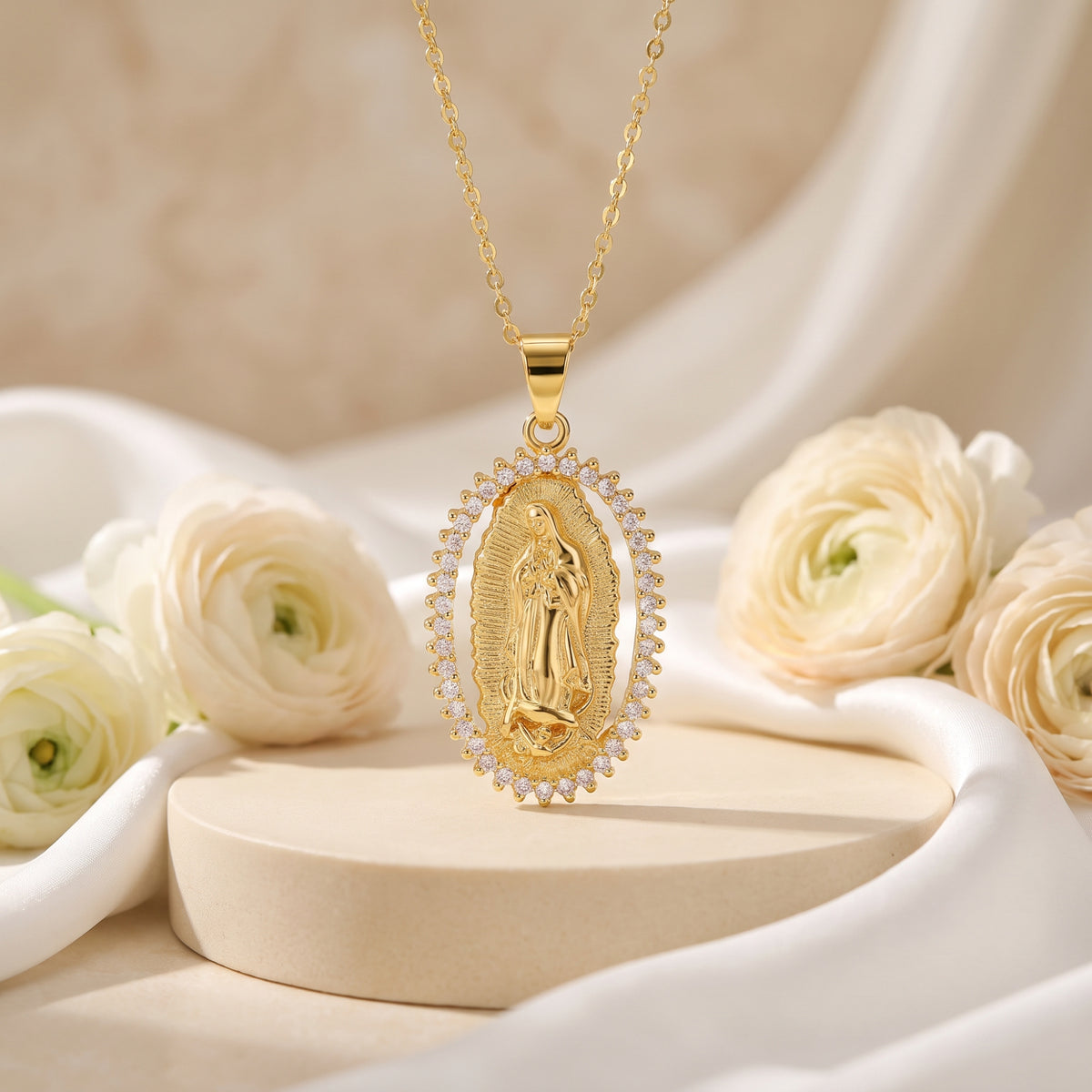 Gold-tone Guadalupe oval pendant necklace with cubic zirconia halo hanging above a pedestal and white roses.