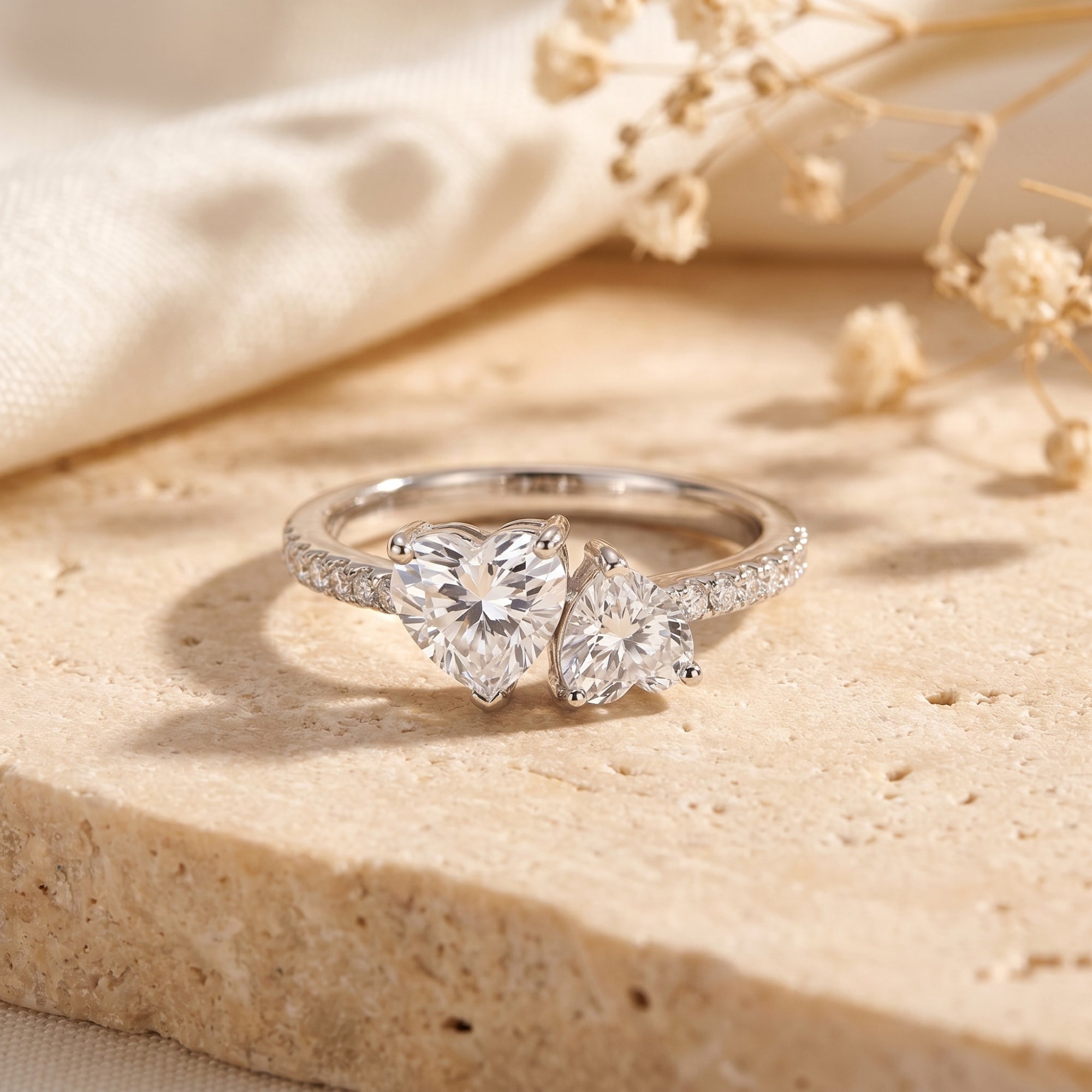 Silver Toi et Moi ring with two heart-cut moissanite stones on a stone surface with flowers.
