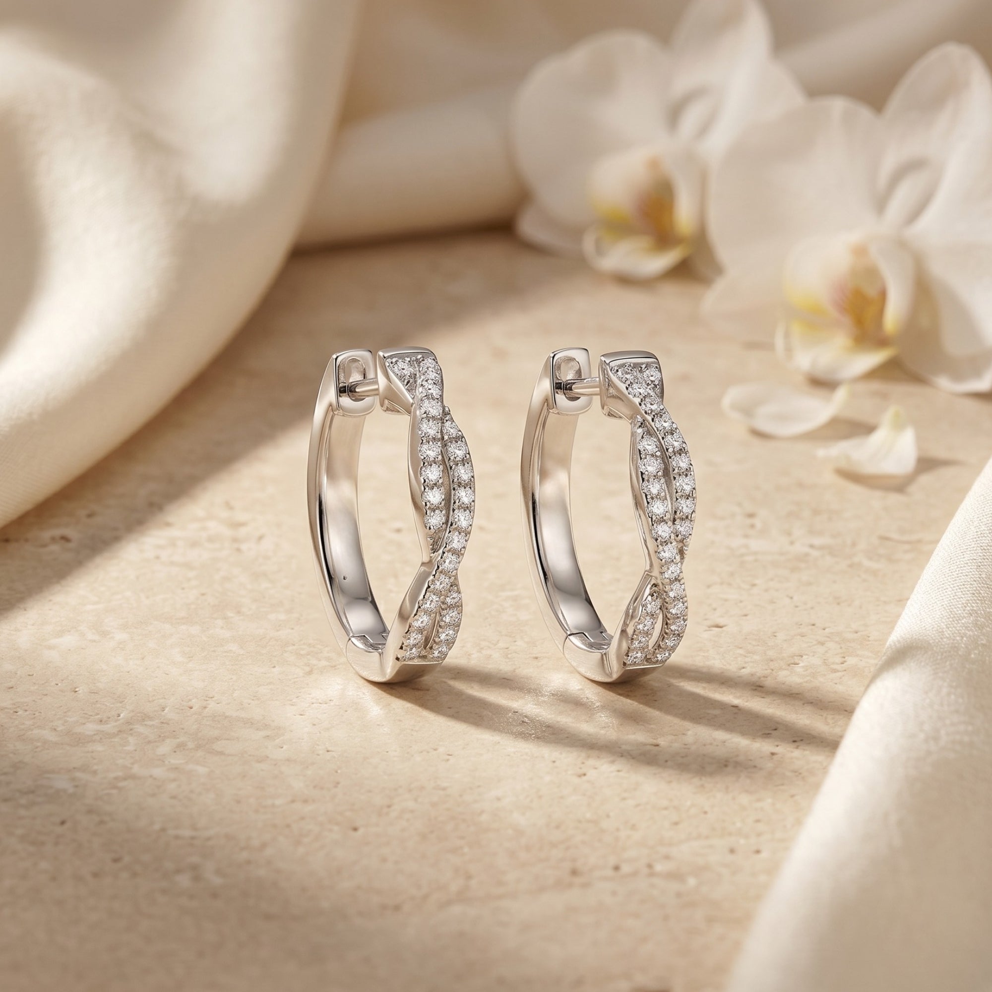 Silver moissanite twisted hoop earrings on stone with white flowers.