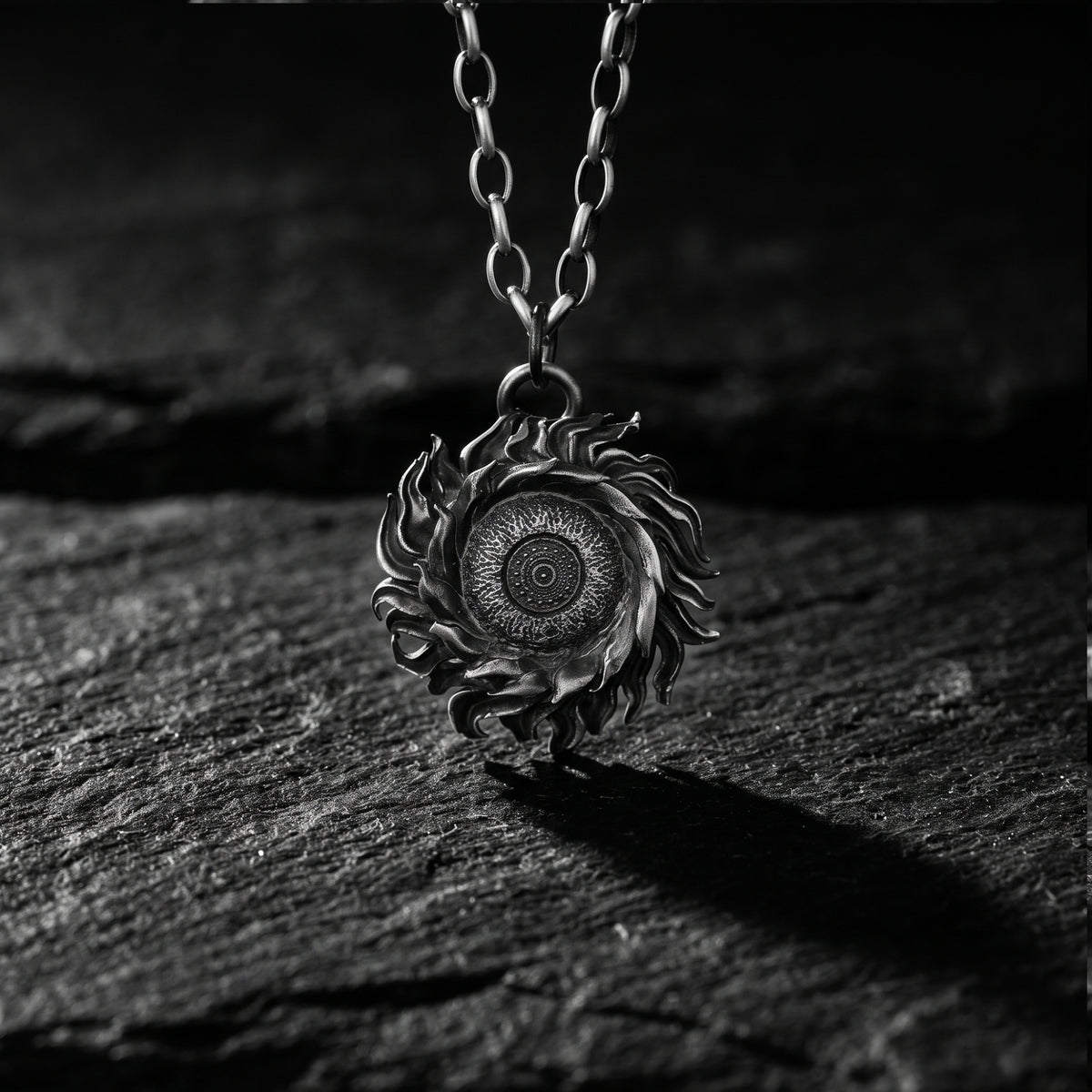 Upright close-up of the silver solar flare pendant suspended on a chain against dark stone.