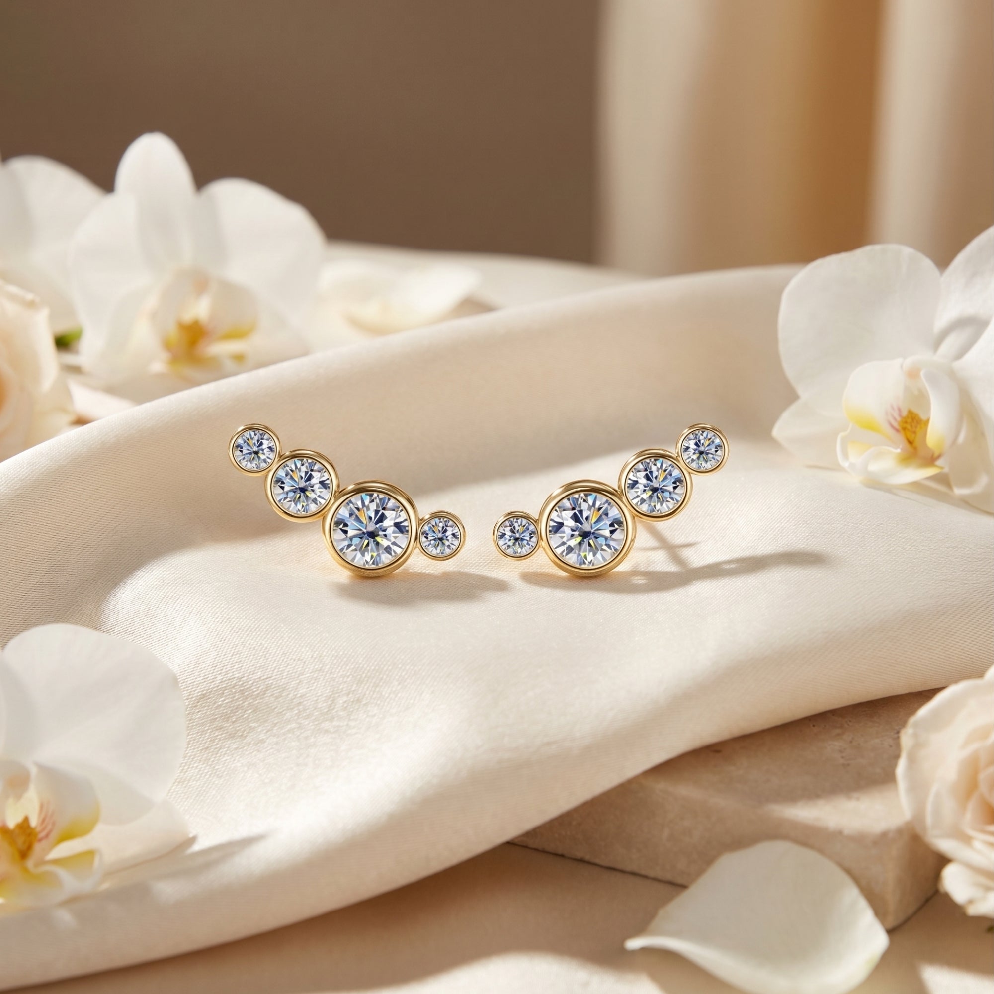 Gold climber earrings with round-cut moissanite stones displayed on white silk fabric with orchids.