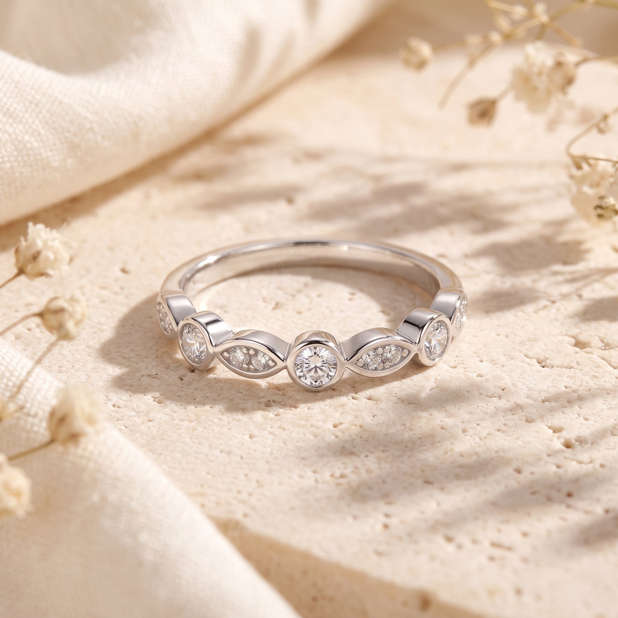 Sterling silver bezel-set cubic zirconia eternity ring on a textured stone surface with floral accents.