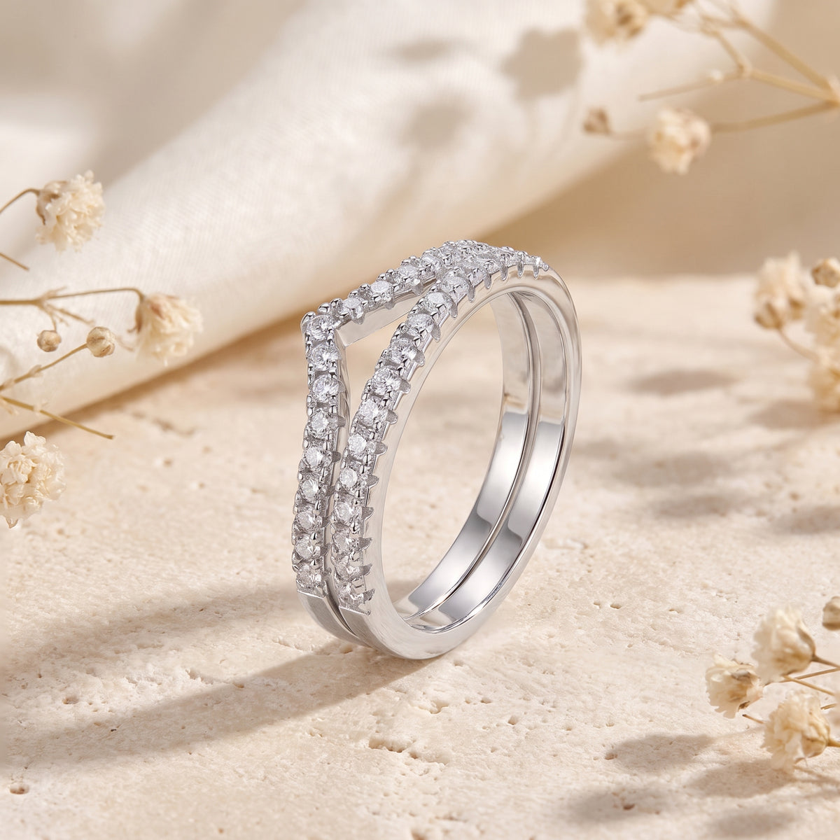 Angled studio view of a silver double chevron ring set with pavé clear stones resting on textured stone.