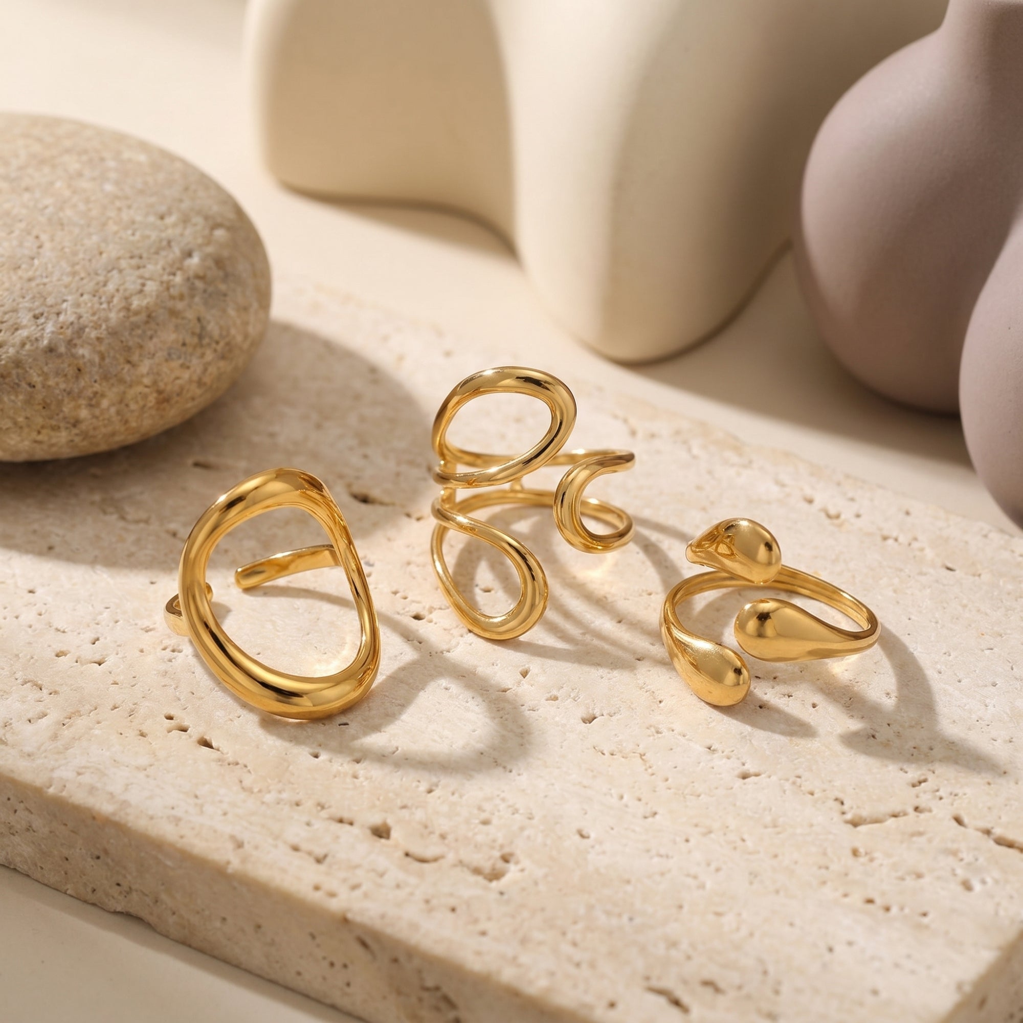 Gold sculptural adjustable ring set on a stone surface with lifestyle props.