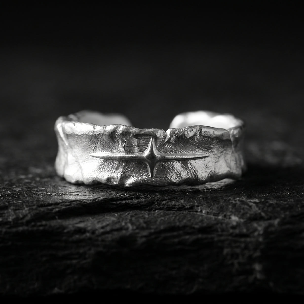 Textured silver open-band ring with a central four-point starburst, displayed on dark slate.