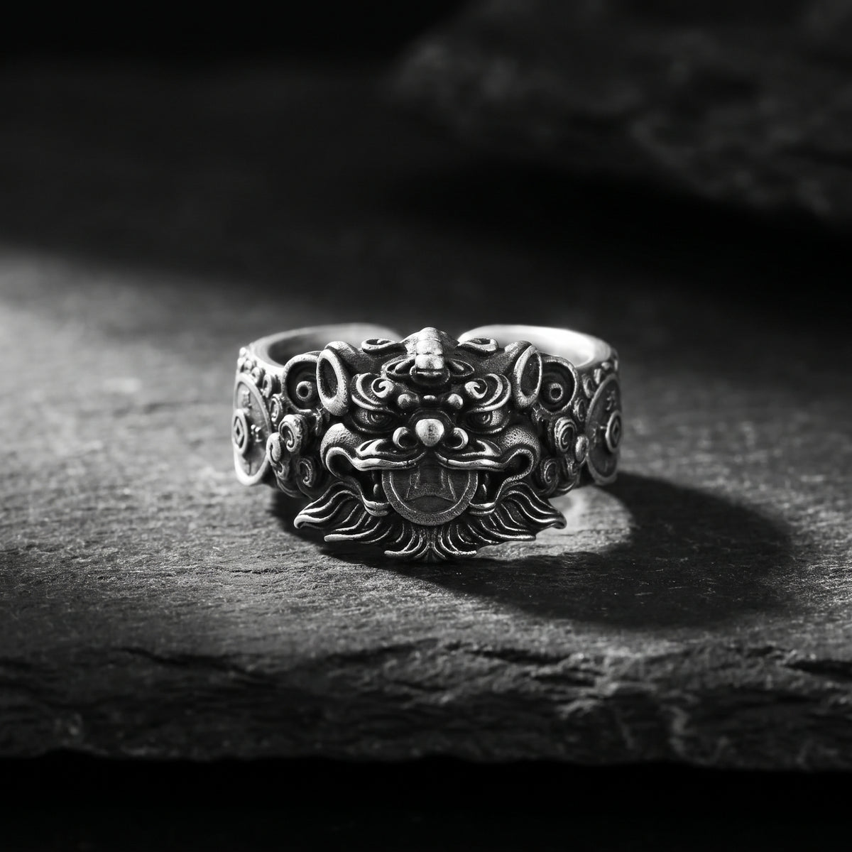 Front view of an antiqued silver Pixiu ring with a sculpted guardian lion holding a coin, displayed on dark rock.
