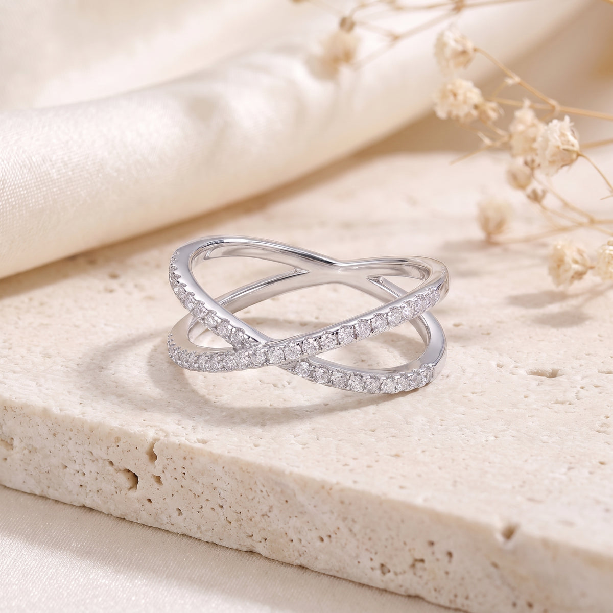 Silver crossover ring with stone-paved bands resting on a light textured stone surface.