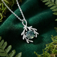 Detail of a natural moss agate stone in a solid gold branch pendant on green velvet.