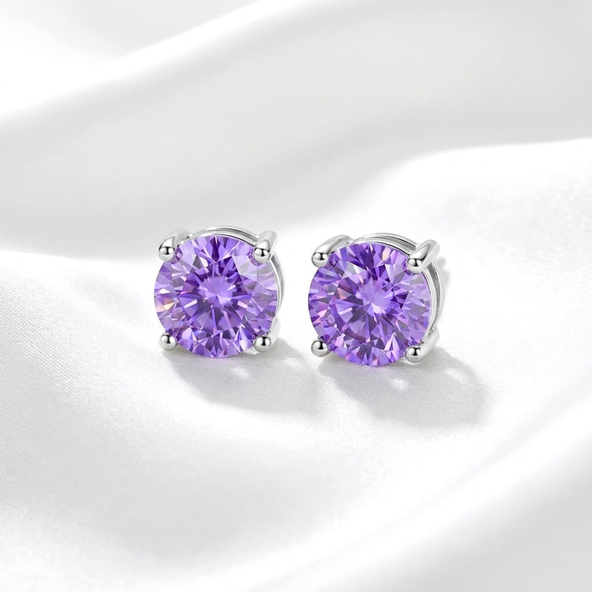 Round cut simulated amethyst stud earrings in sterling silver on a white draped fabric background.