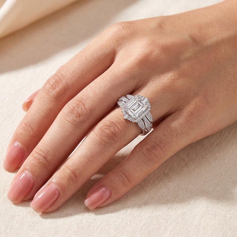 Silver halo ring with an emerald-cut center stone shown worn on a hand.