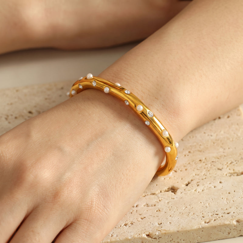 Close-up of the gold-tone pearl and cubic zirconia open cuff bracelet worn on a wrist over stone.