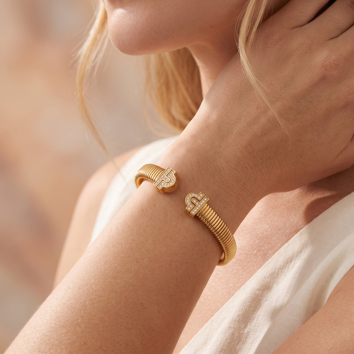 Gold-finish ribbed open cuff bracelet with pavé ends worn on a wrist beside a white garment.