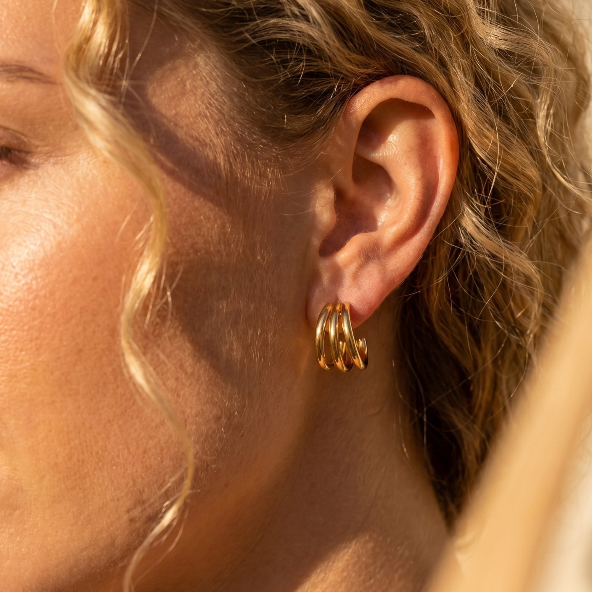 18K gold PVD triple-band hoop earring worn on a model's ear.
