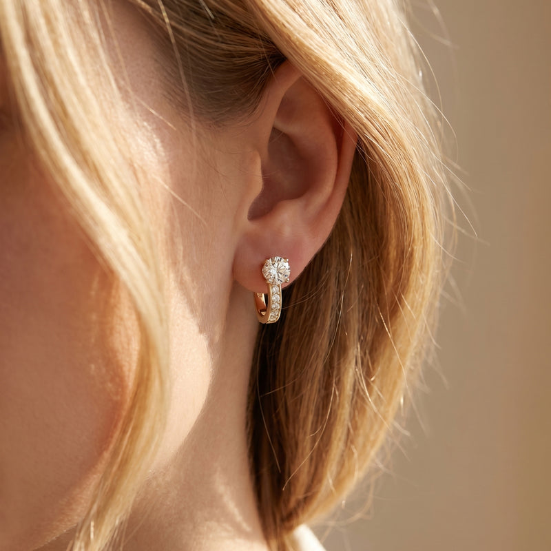 Gold moissanite hoop earring with a round cut center stone shown on a model's ear.