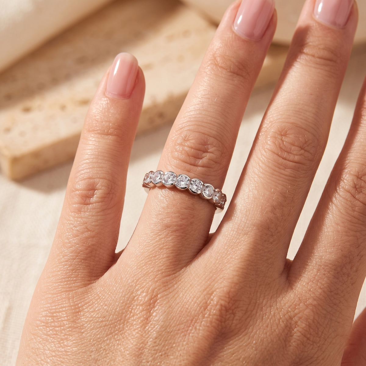 The Zarielle sterling silver bezel eternity ring with round simulated diamonds worn on a woman's finger.