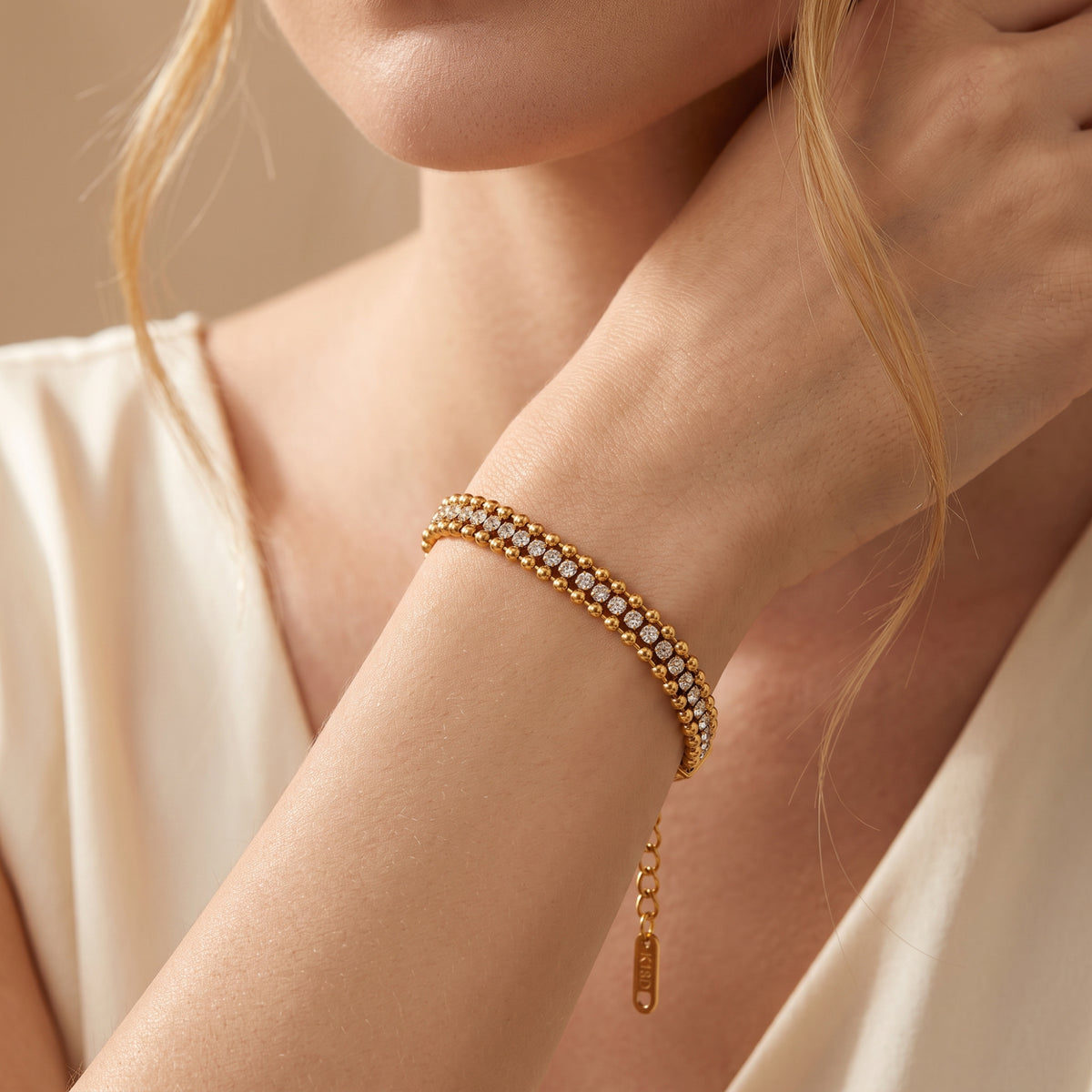 Model wearing a gold-tone triple-row beaded bracelet with cubic zirconia, with a hand near the neck.