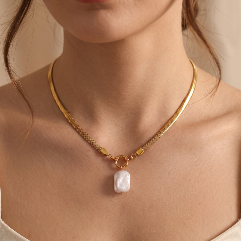 Front view of a woman wearing the gold herringbone snake chain necklace with a white baroque pearl pendant.