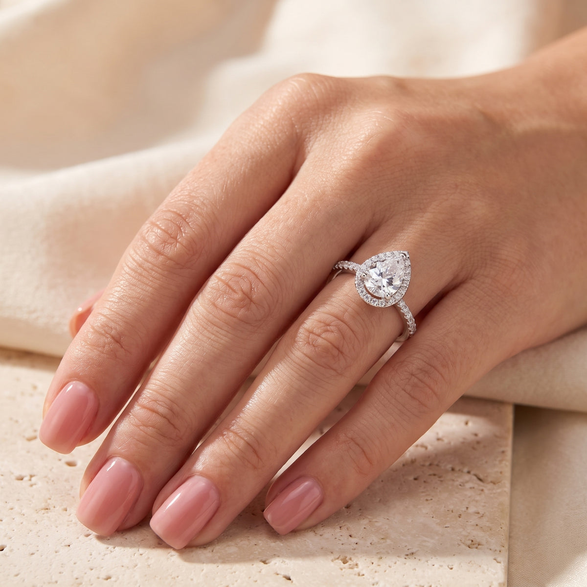 Hand wearing the silver ring with a pear-cut halo center stone and pavé accents along the band.