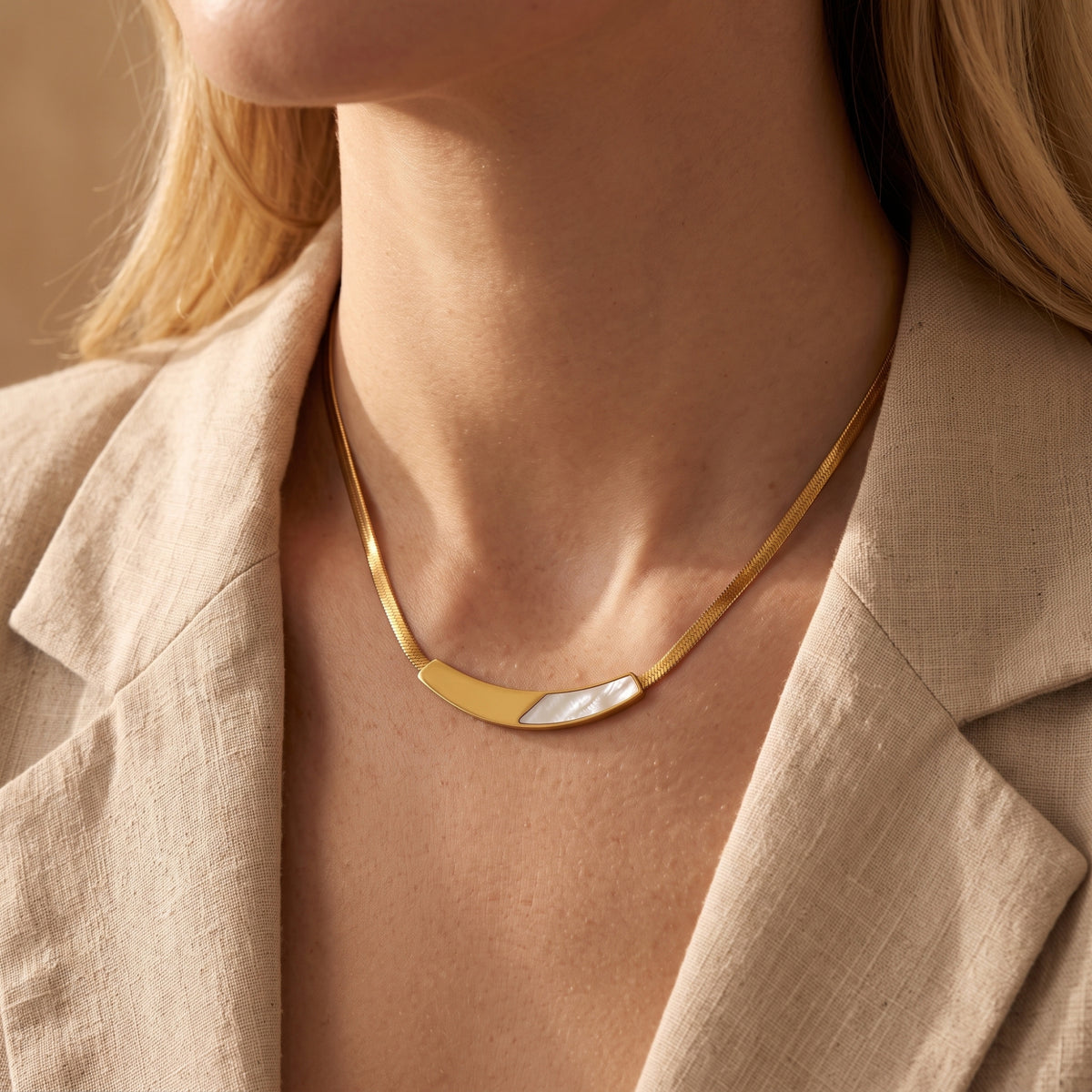 Gold flat snake chain necklace with mother of pearl accent worn by a model in a beige blazer.