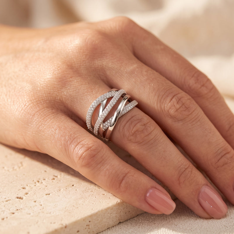 Silver multi-row crossover ring with simulated diamonds worn on a finger.