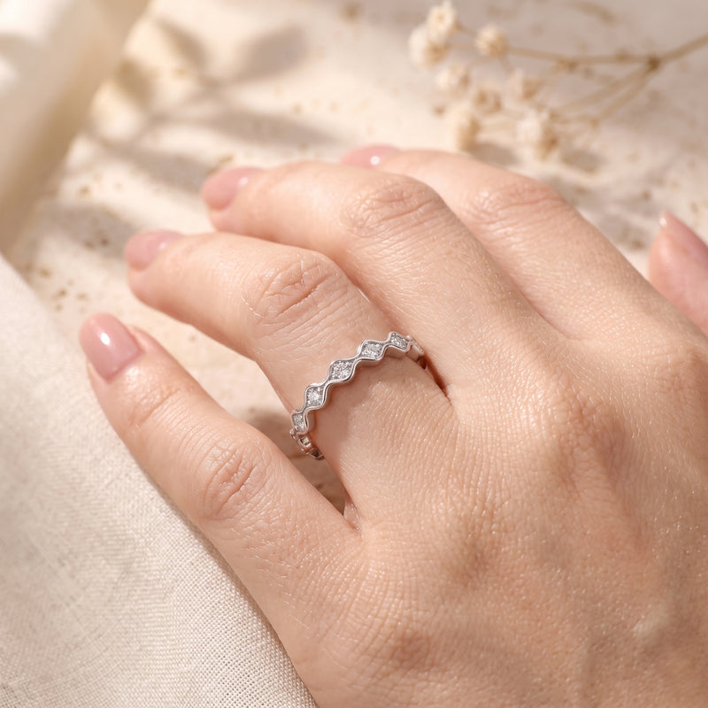 Wavy silver simulated diamond ring worn on a finger against a soft fabric background.