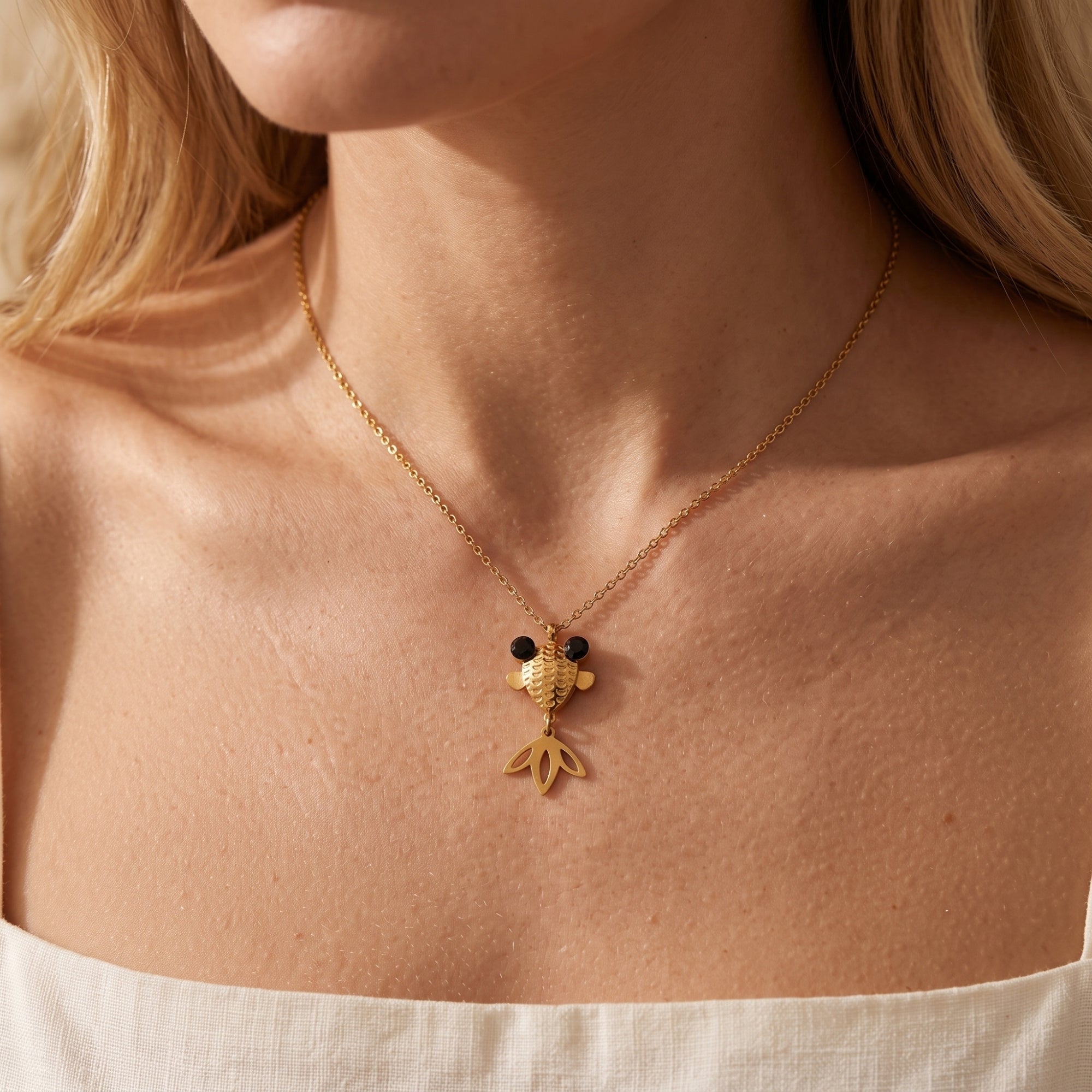 Gold finish goldfish pendant necklace with black stone eyes worn on a model's neck.