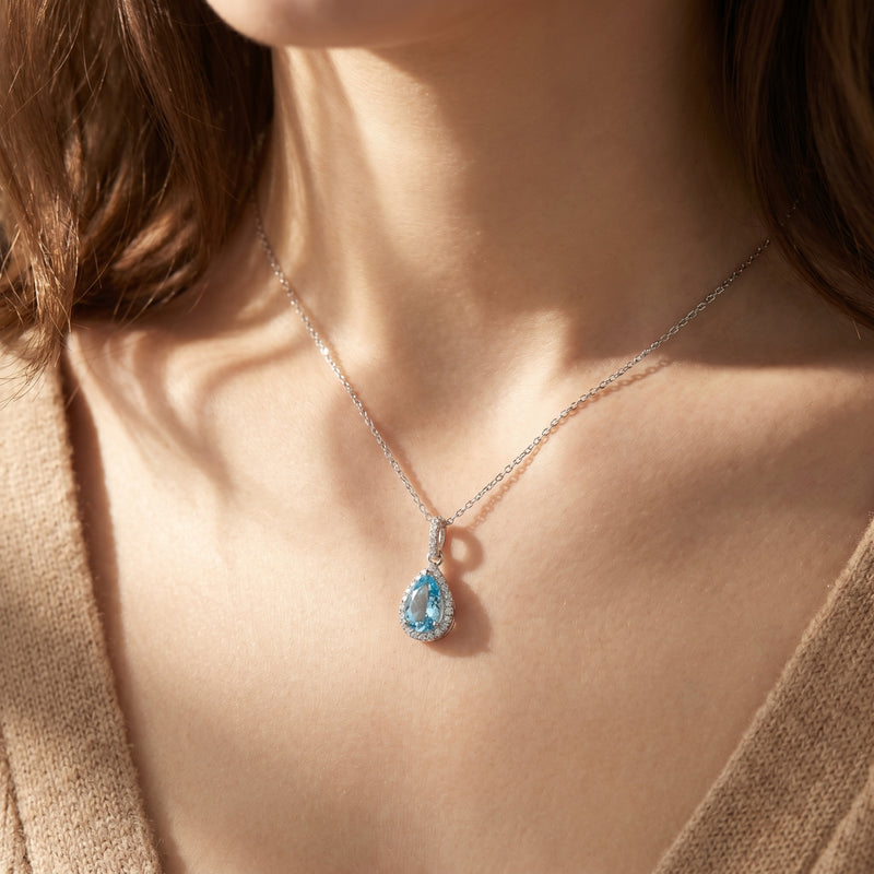 Woman wearing the pear-shaped aquamarine halo necklace in sterling silver.